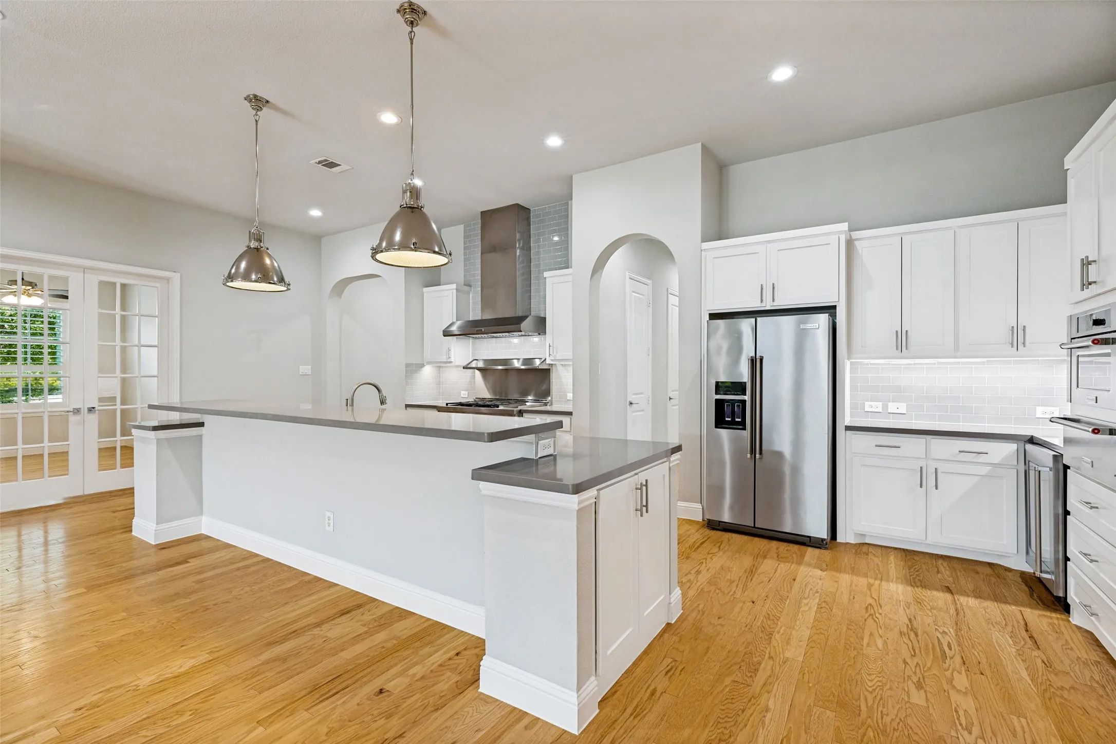 Gourmet kitchen with wood-finish flooring, white cabinetry, a large island with a countertop, stainless steel appliances, and pendant lighting