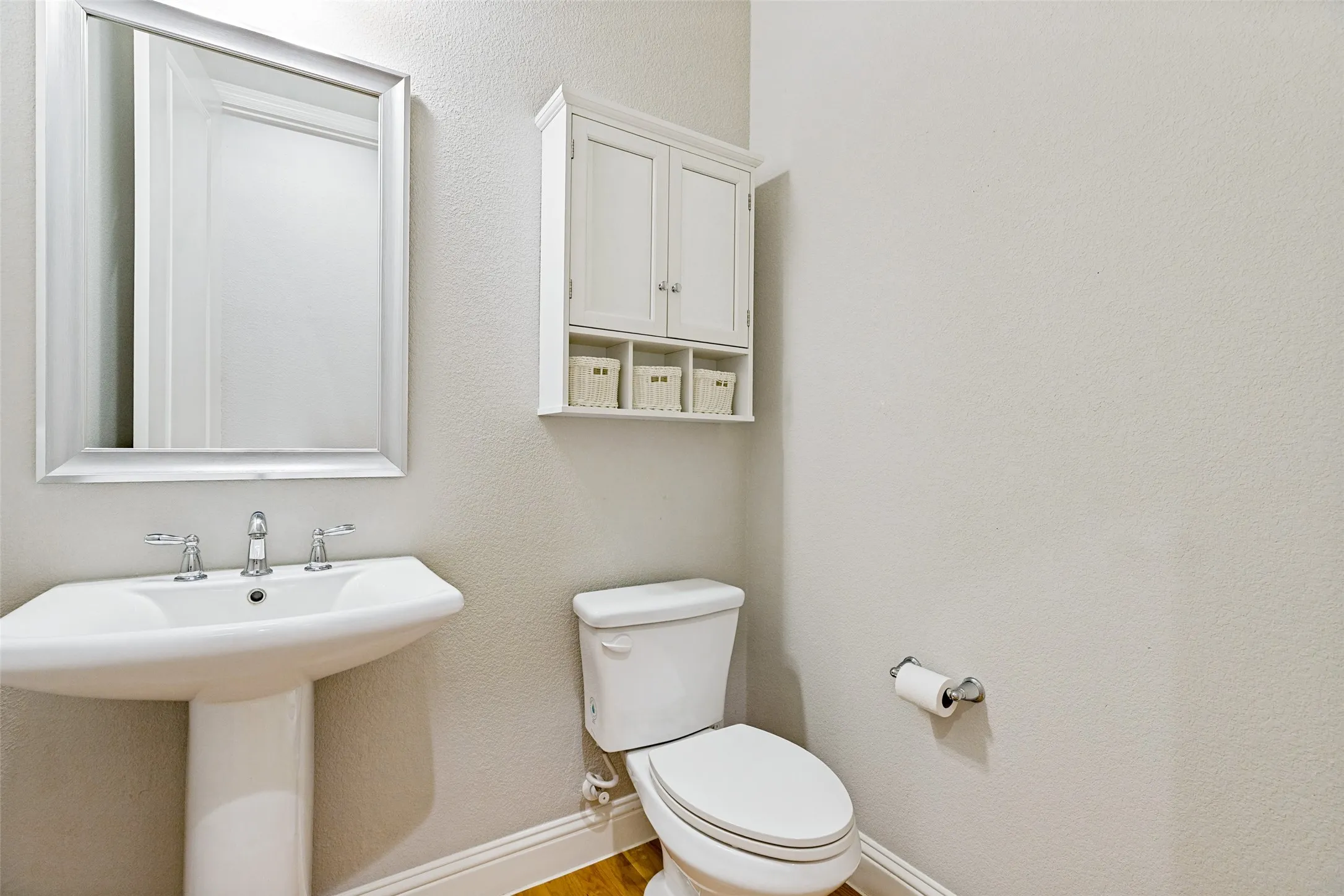Pedestal sink with chrome fixtures, framed mirror, wall-mounted storage cabinet, and wood-finish flooring