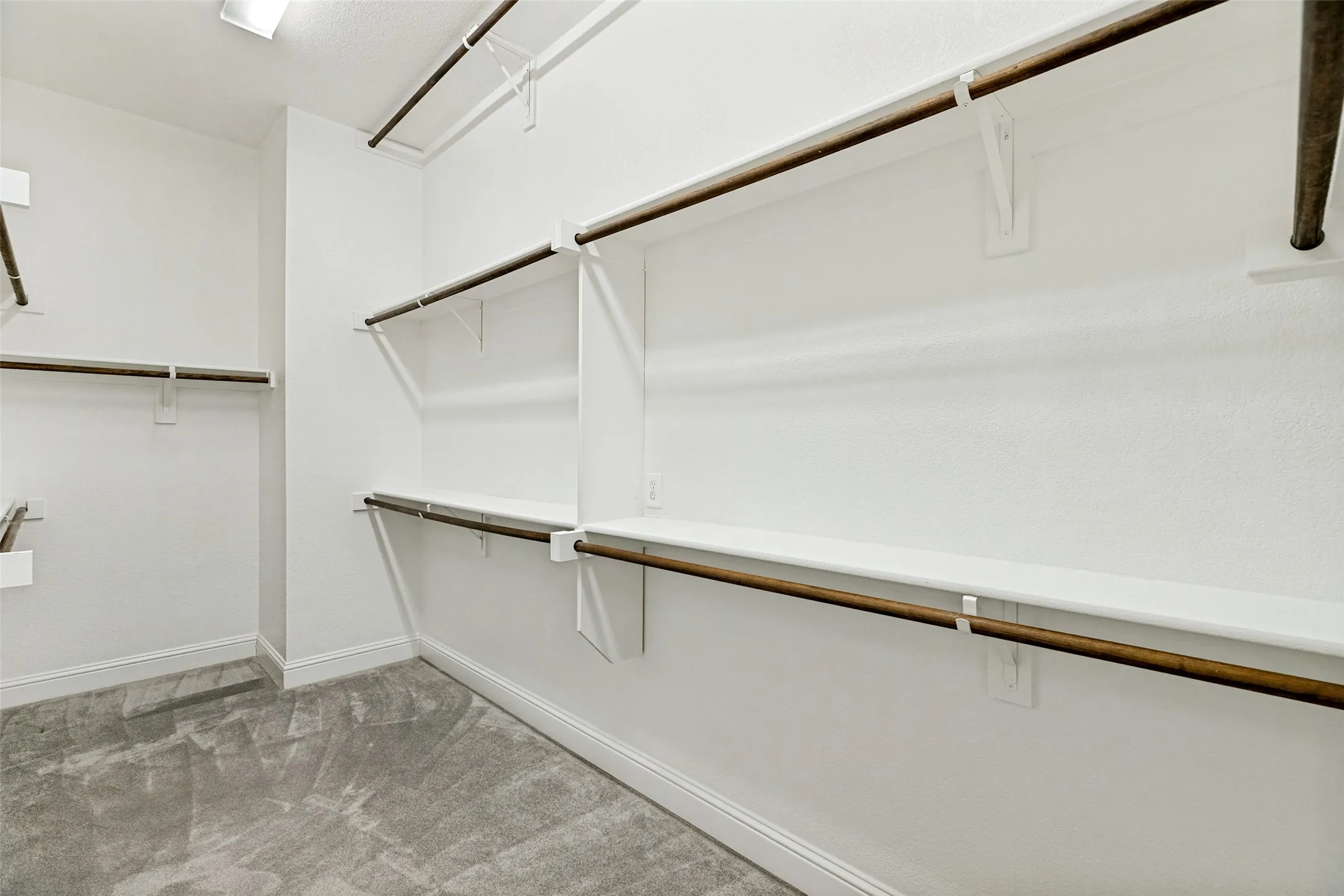 Recessed overhead lighting, textured white walls, extensive shelving, multiple hanging rods, and gray carpet flooring