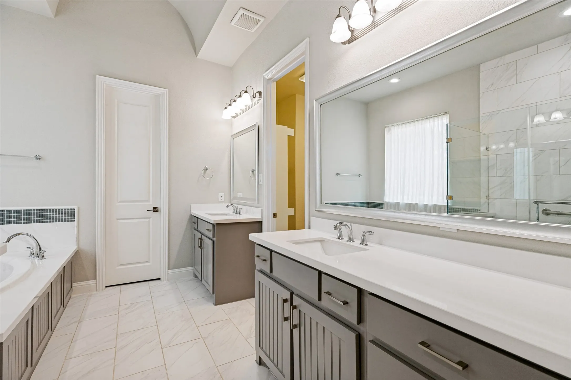Dual vanity sinks with white countertops, white tile flooring, and a built-in tub