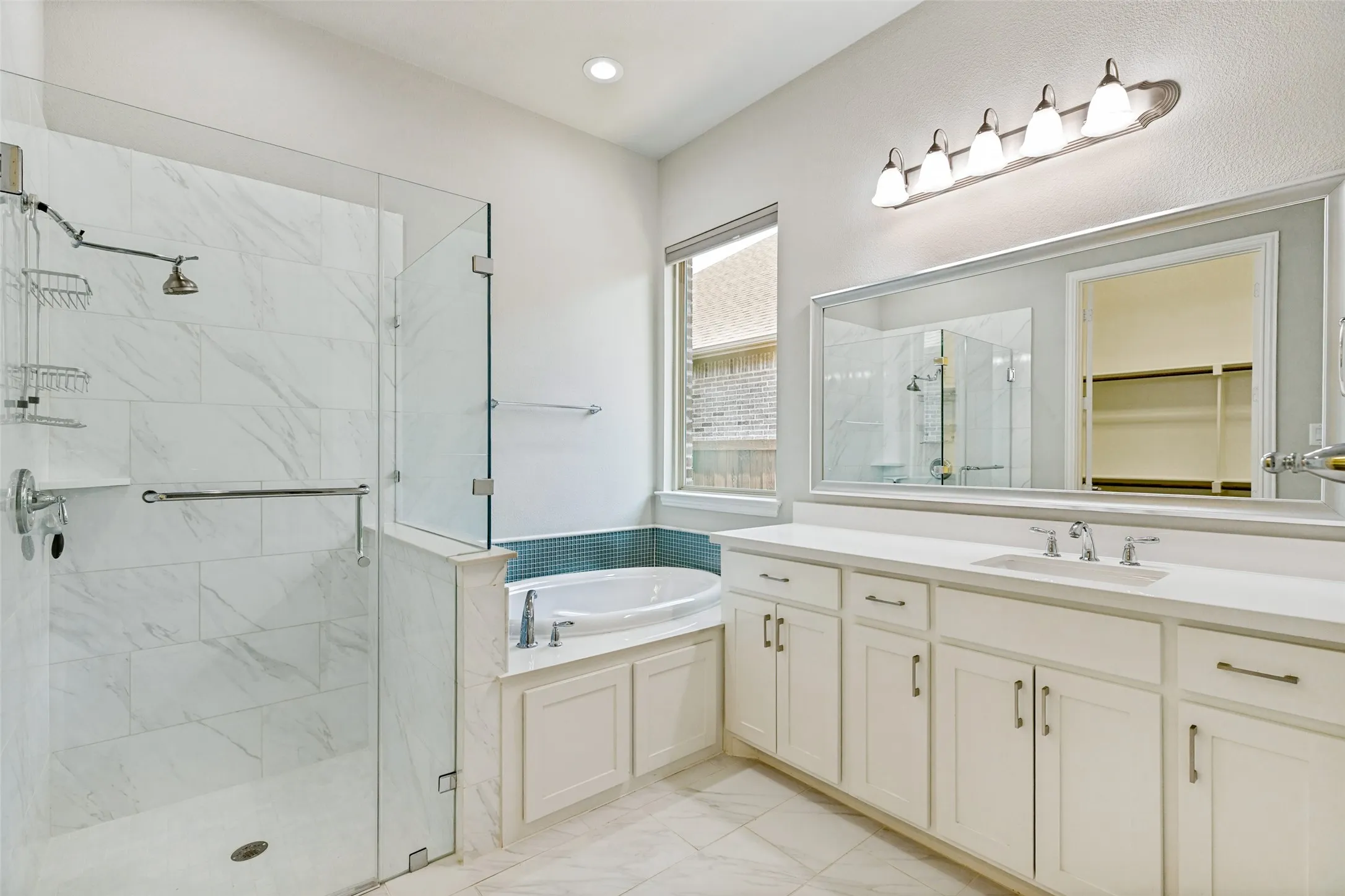 Spacious bathroom featuring a frameless glass shower enclosure, a separate built-in soaking tub with tile surround, a long vanity with dual sinks, and a large wall-mounted mirror