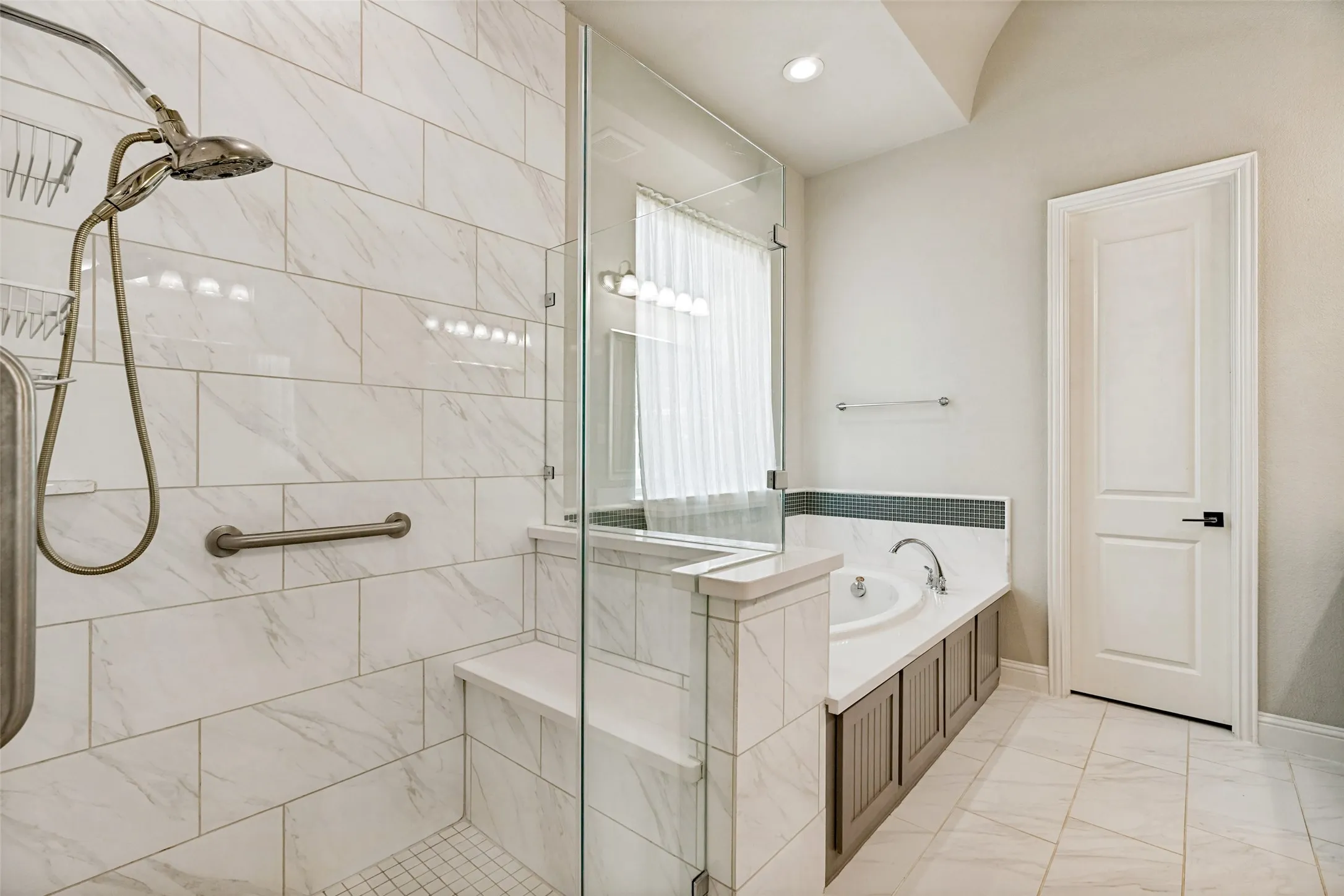 Glass-enclosed shower with a built-in bench, a separate soaking tub, and a white paneled door