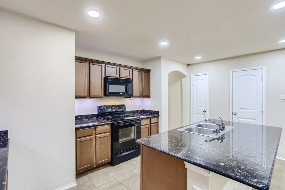 Kitchen featuring an integrated island with a double basin sink, dark stone-finish countertops, warm wood cabinetry, and a black range with an overhead microwave