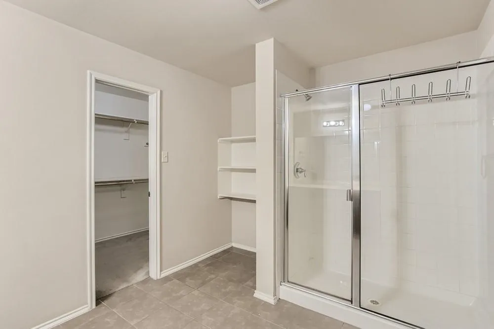 Walk-in closet with built-in shelving, glass-enclosed shower with tile surround, and tiled flooring