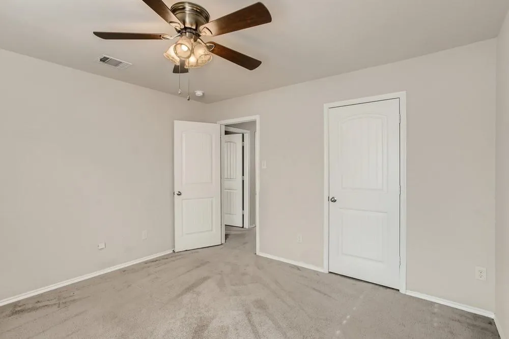 Light gray wall paint, textured carpet flooring, ceiling fan with integrated lighting, and white paneled doors