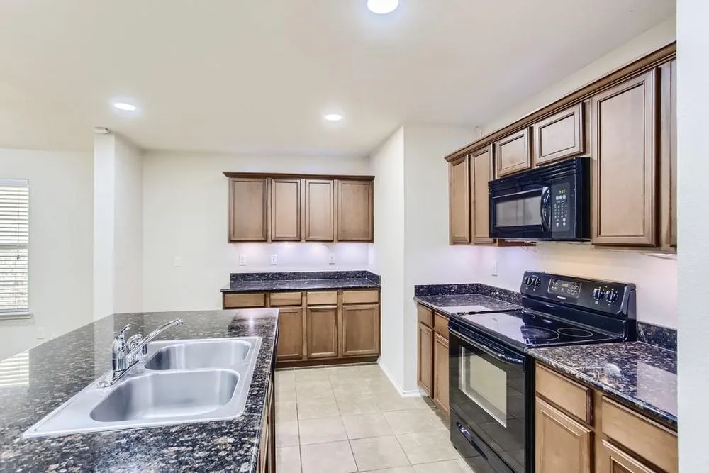 Kitchen featuring dark cabinetry, dark speckled countertops, a stainless steel double basin sink, and black appliances