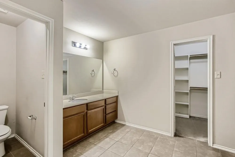 Vanity with integrated sink, wood-finish cabinetry, and a large wall mirror