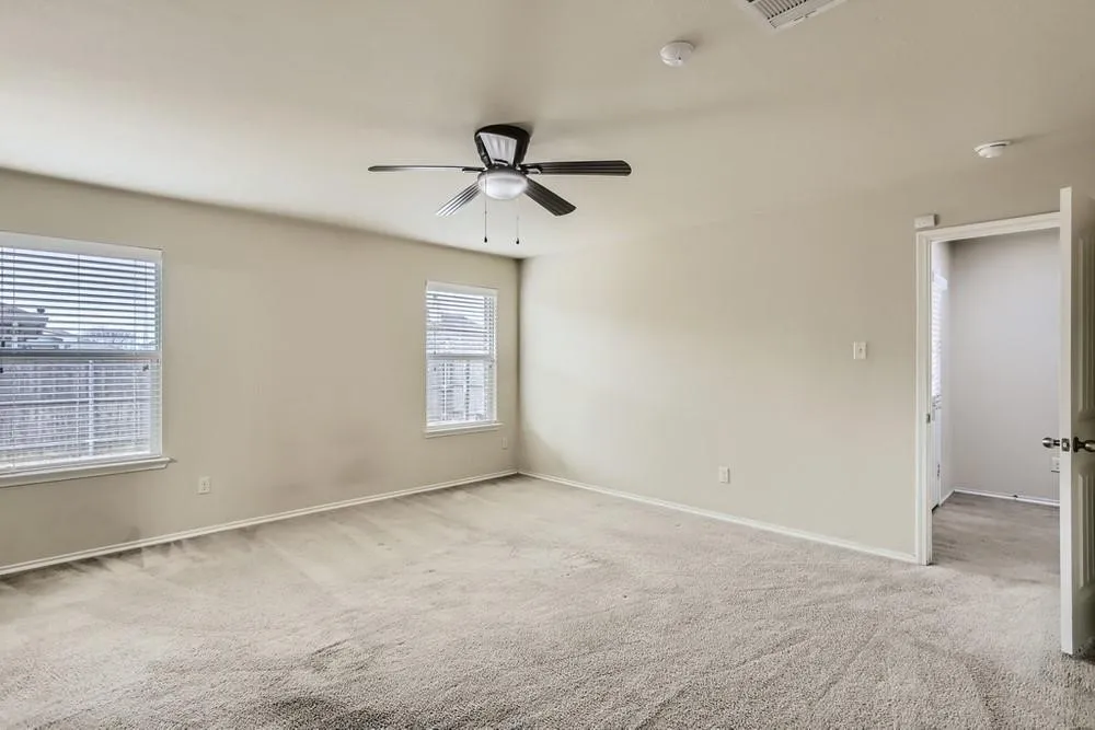 Spacious room featuring carpet flooring, two windows with blinds, a ceiling fan with integrated lighting, and neutral wall tones