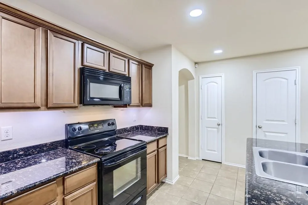 Kitchen featuring dark wood-finish cabinetry, black appliances, dark speckled countertops, and a double basin stainless steel sink