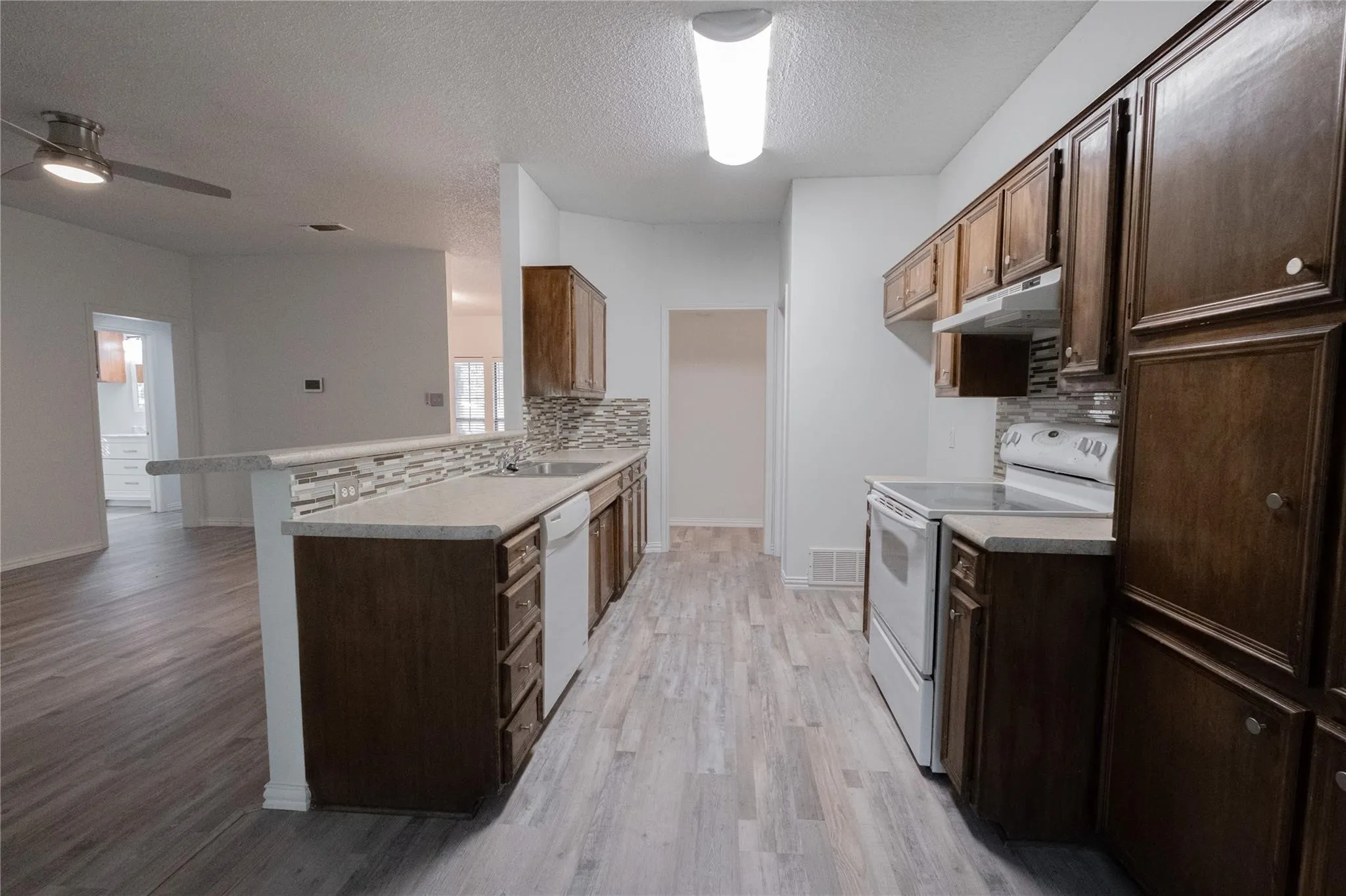 Kitchen featuring wood-finish flooring, wood cabinetry, white appliances, light countertops, and a tile backsplash
