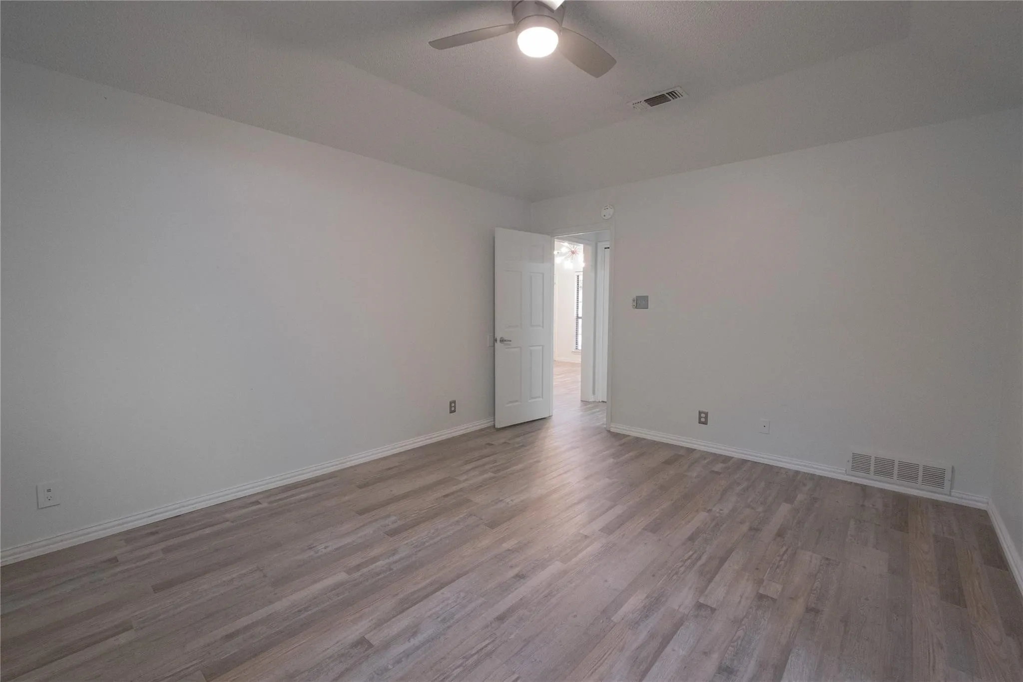 Spacious room featuring wood-finish flooring, light-toned walls, a ceiling fan with integrated lighting, and a white interior door