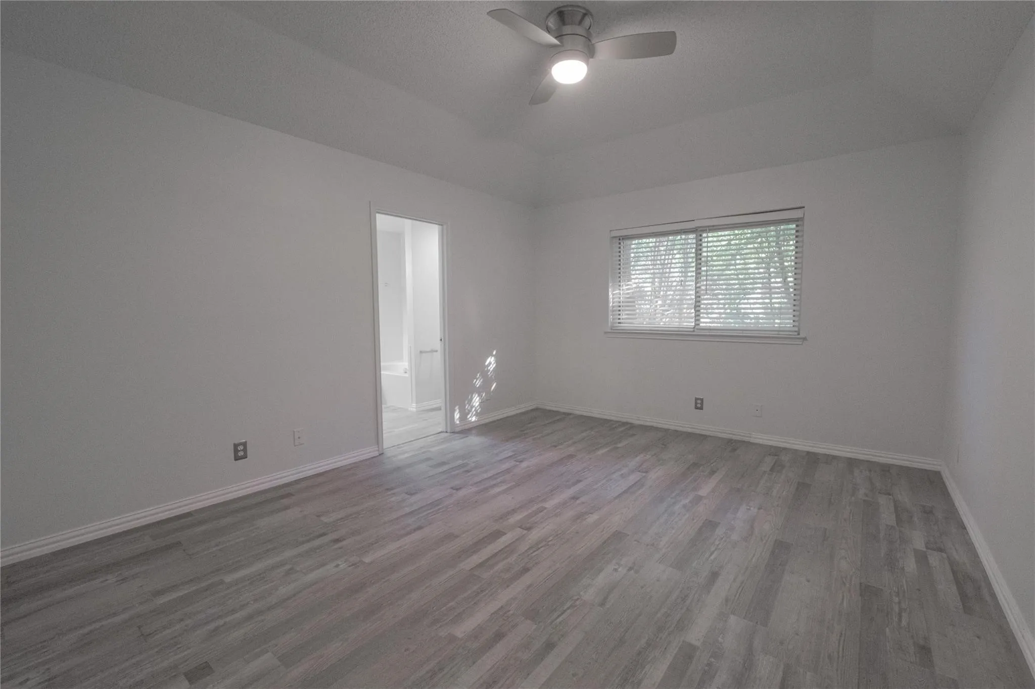 Spacious room with wood-finish flooring, a ceiling fan with integrated lighting, and a large window with horizontal blinds