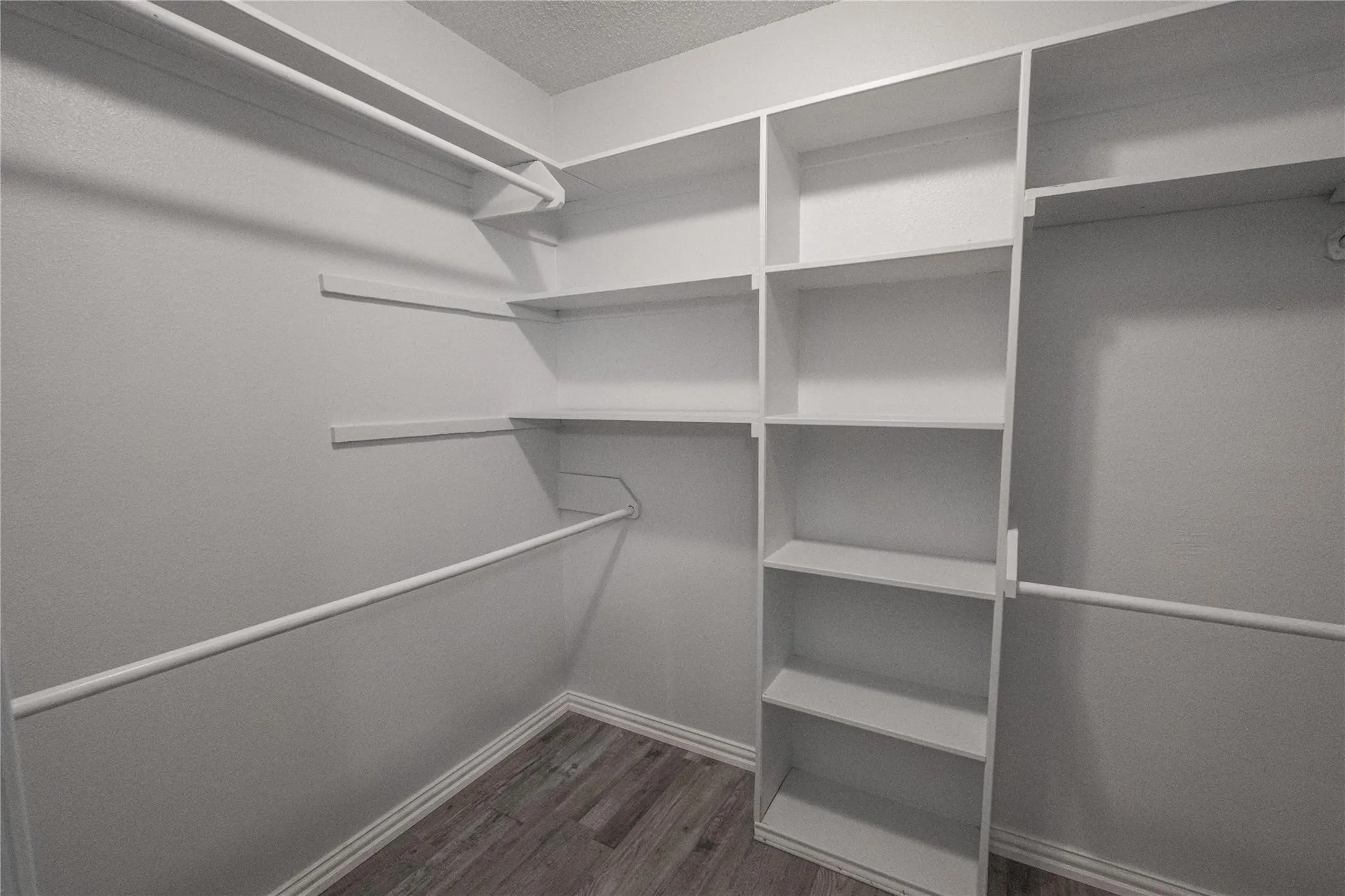 Built-in shelving, multiple hanging rods, and wood-finish flooring