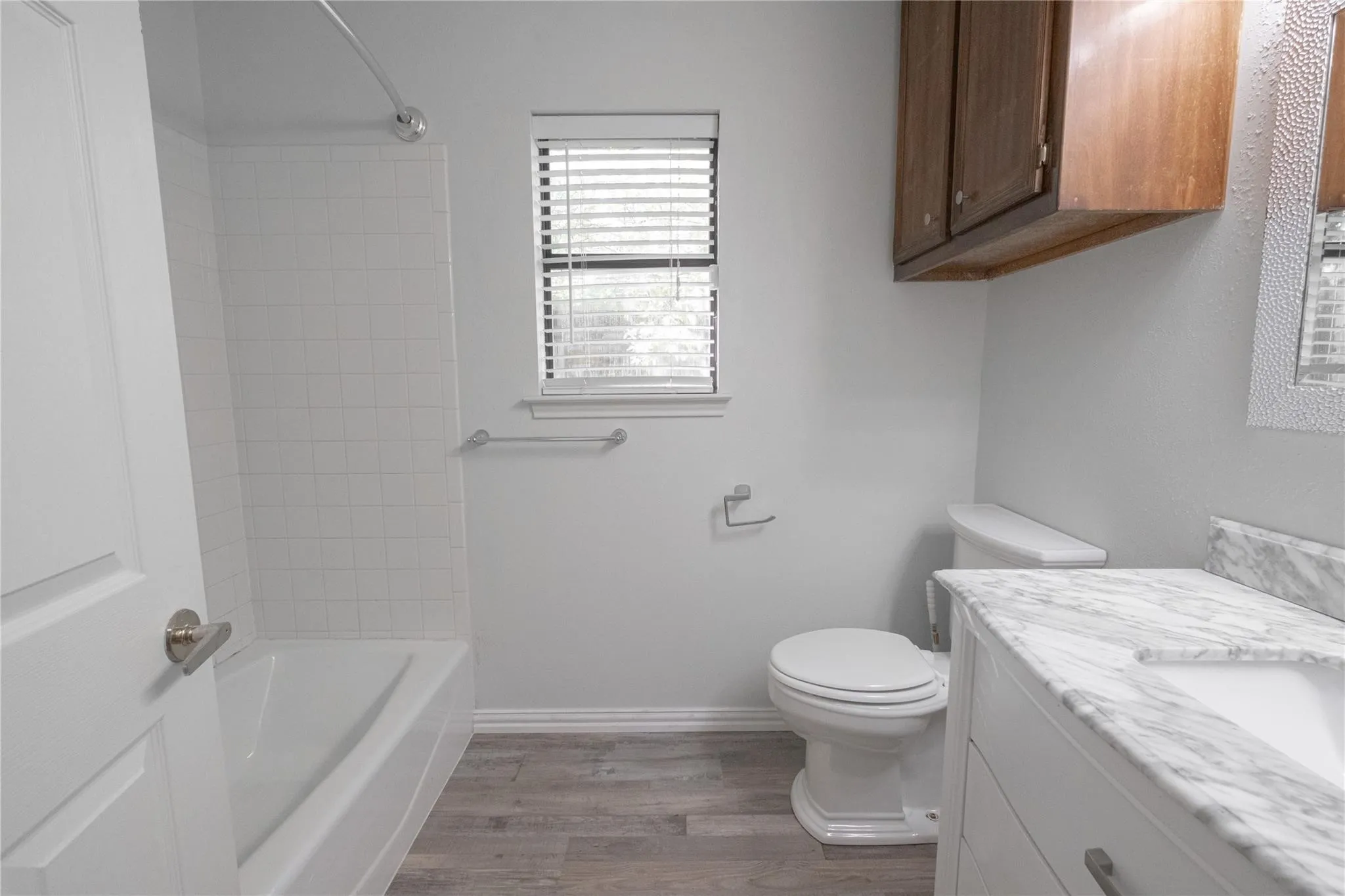 White subway tile shower surround with a built-in tub, wood-finish flooring, white vanity with integrated sink, and a stone-finish countertop