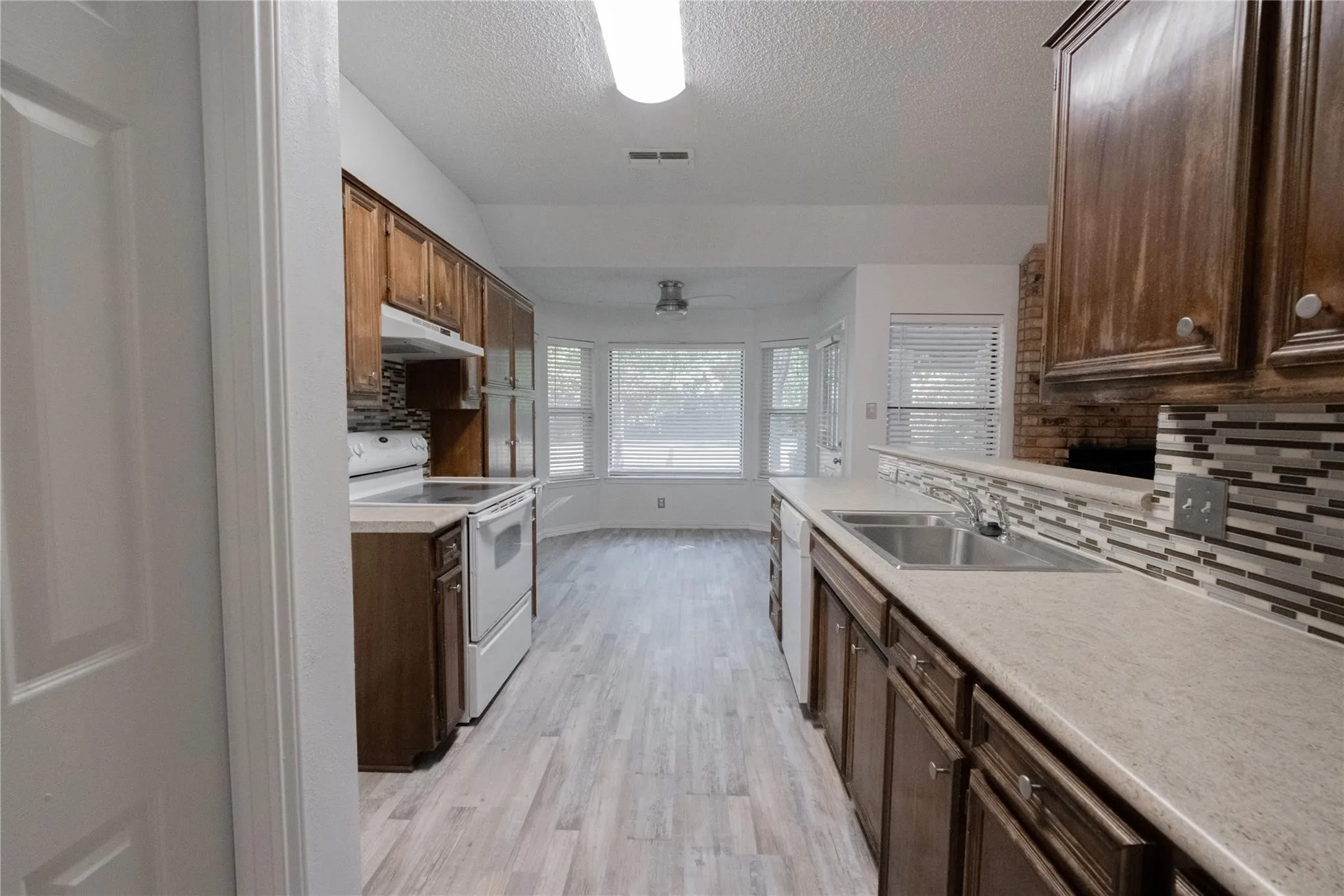 Kitchen featuring wood-finish flooring, wood cabinetry, light-toned countertops, a mosaic tile backsplash, and a bay window