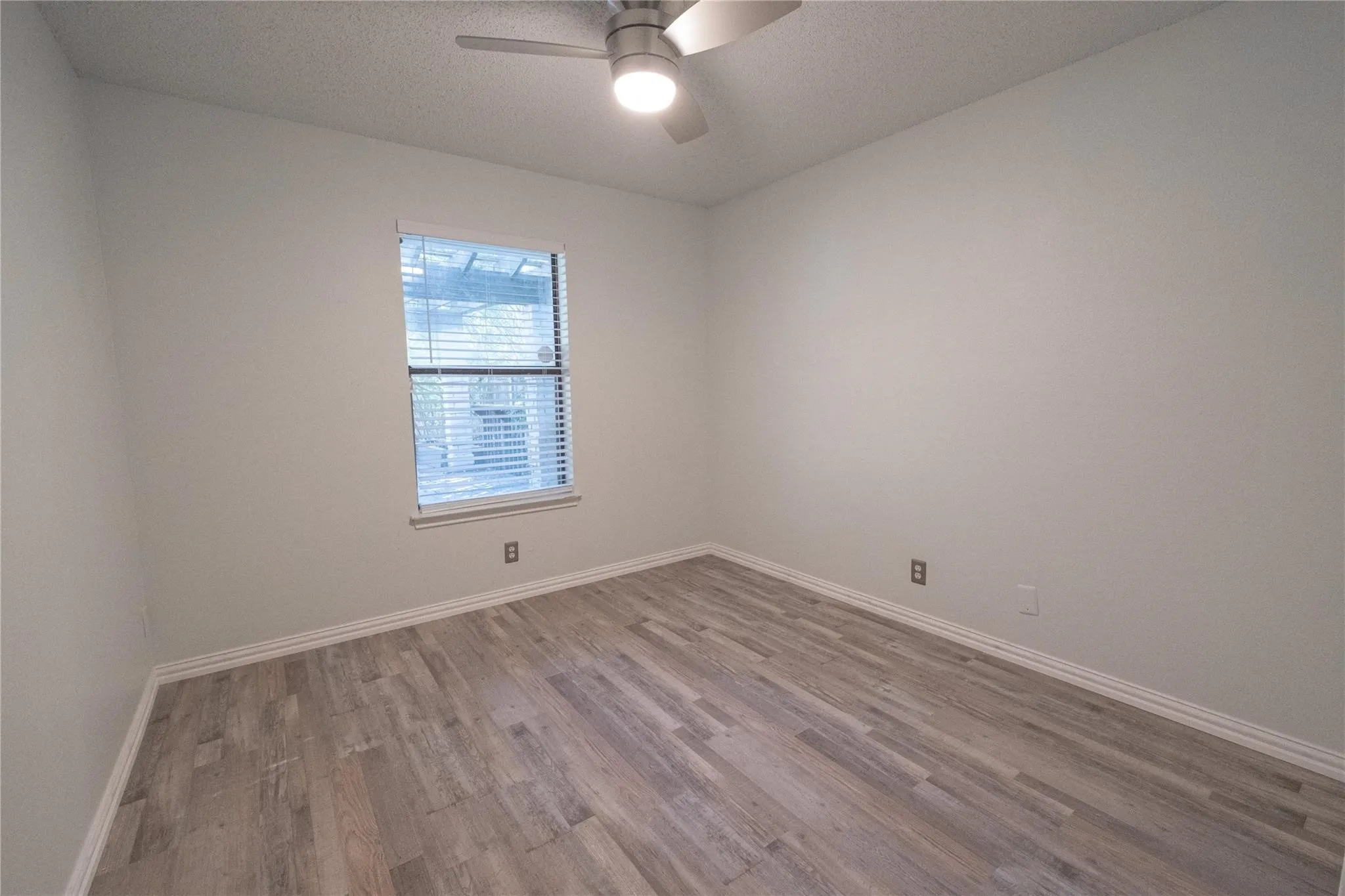 Neutral wall color with wood-finish flooring, a ceiling fan with integrated lighting, and a window with blinds