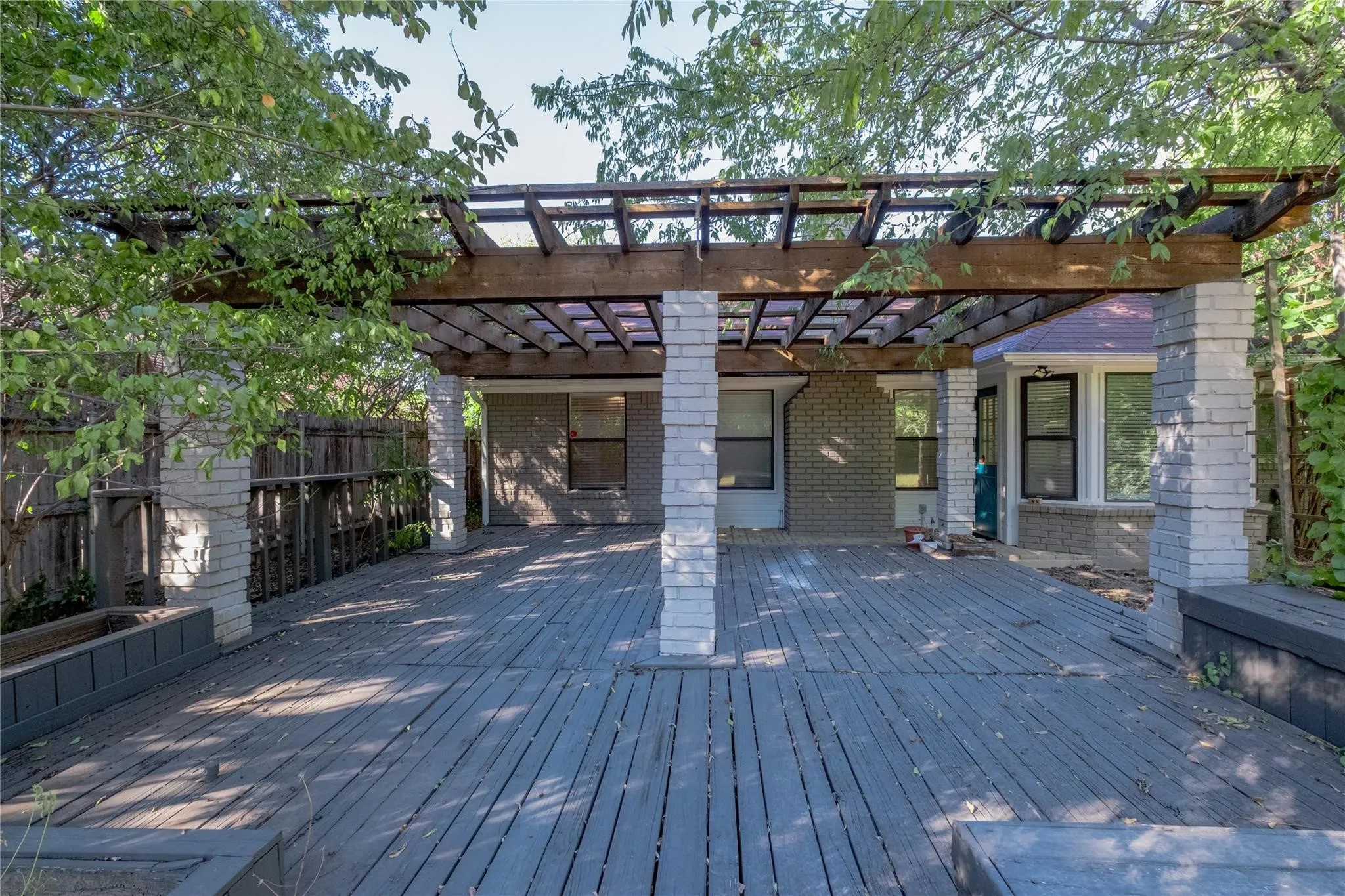 Expansive wood deck with a pergola, supported by brick columns, featuring integrated raised planters
