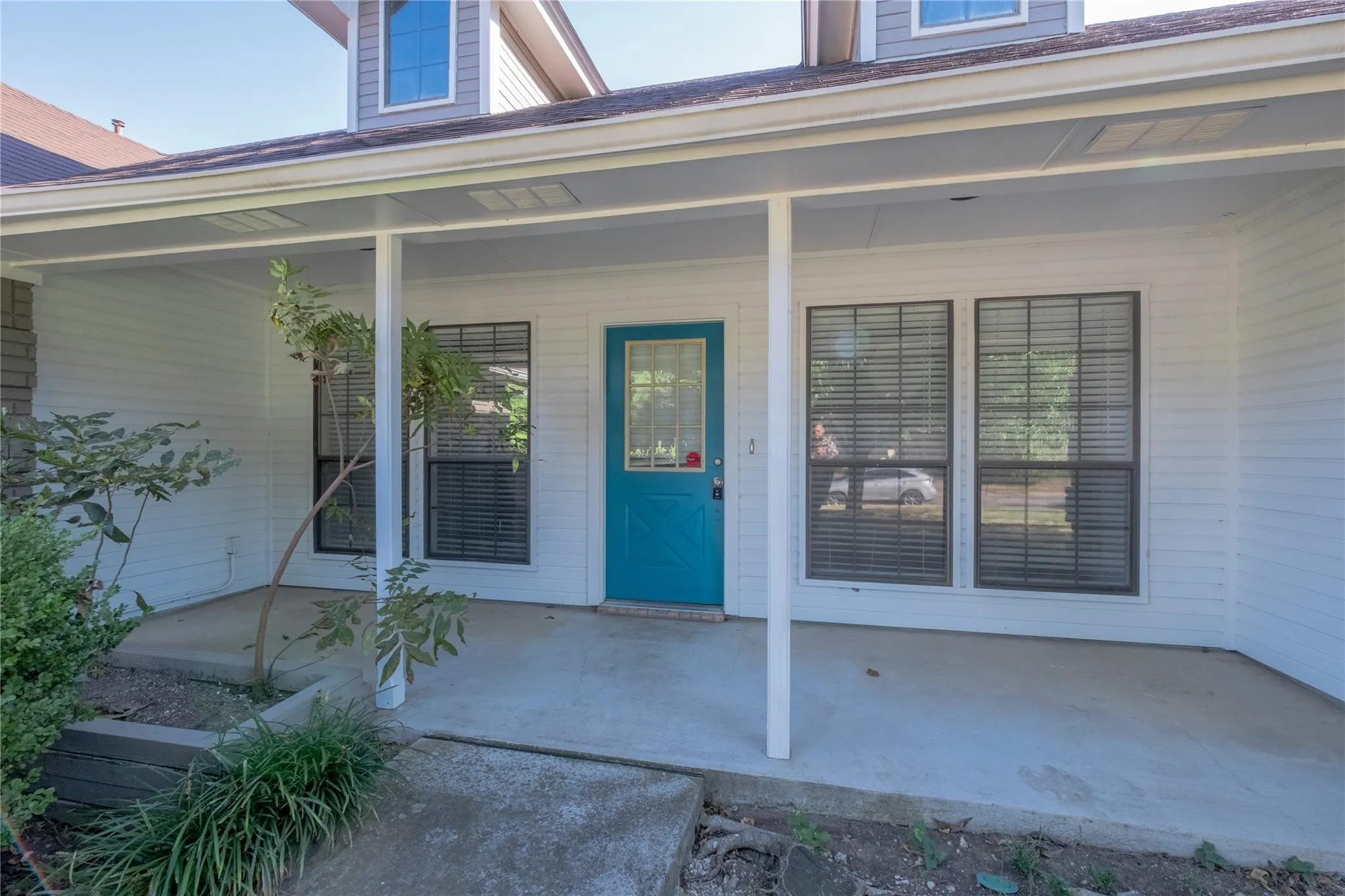 Covered front porch with white siding, a vibrant blue entry door, and multi-pane windows