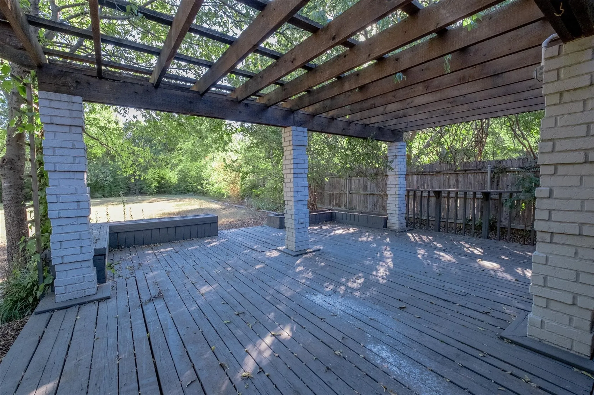 Expansive wood-plank deck with a wood pergola, brick columns, and an integrated wood bench