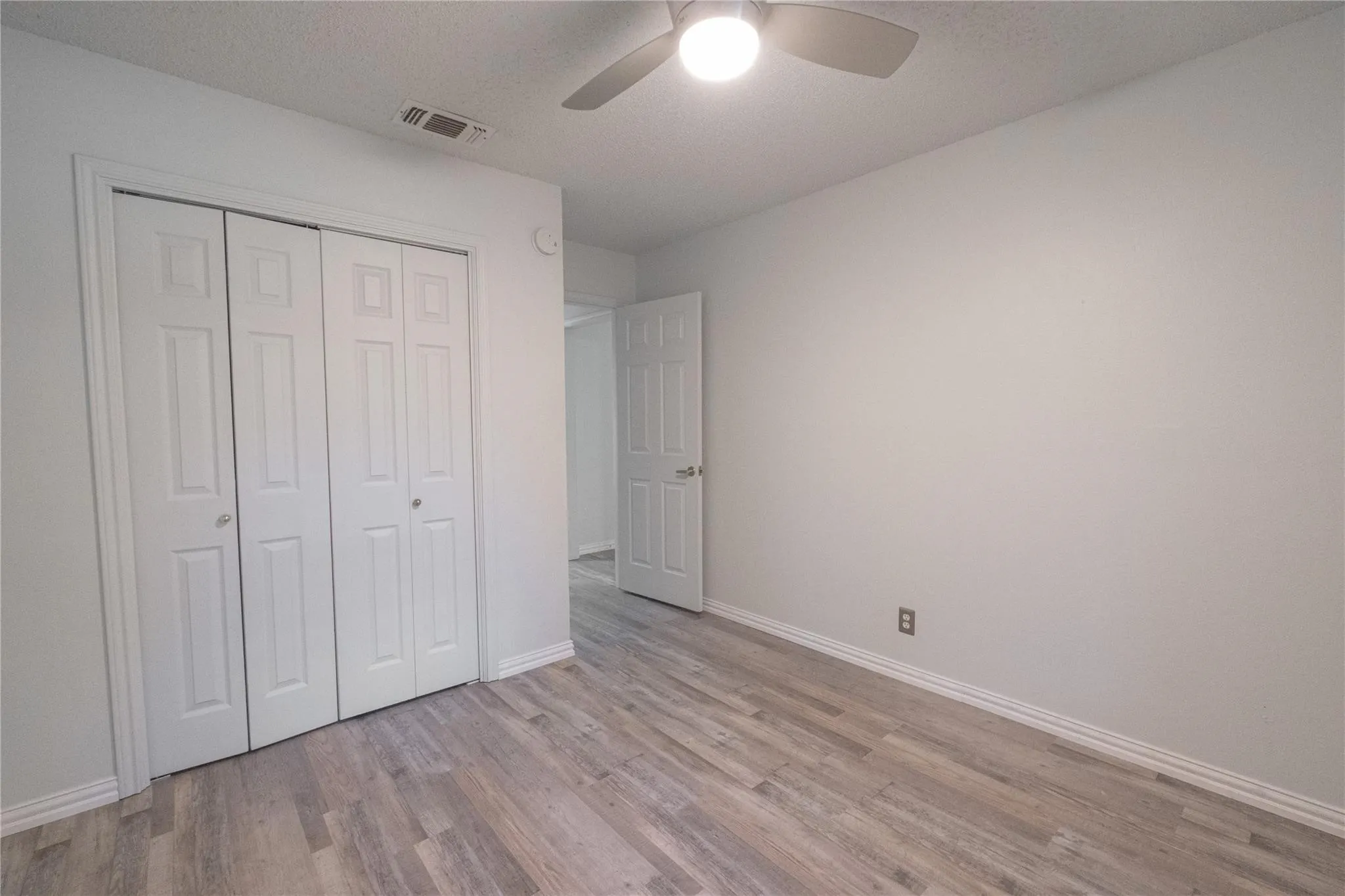 Neutral wall color, wood-finish flooring, ceiling fan with integrated lighting, bi-fold closet doors, and recessed ceiling vent