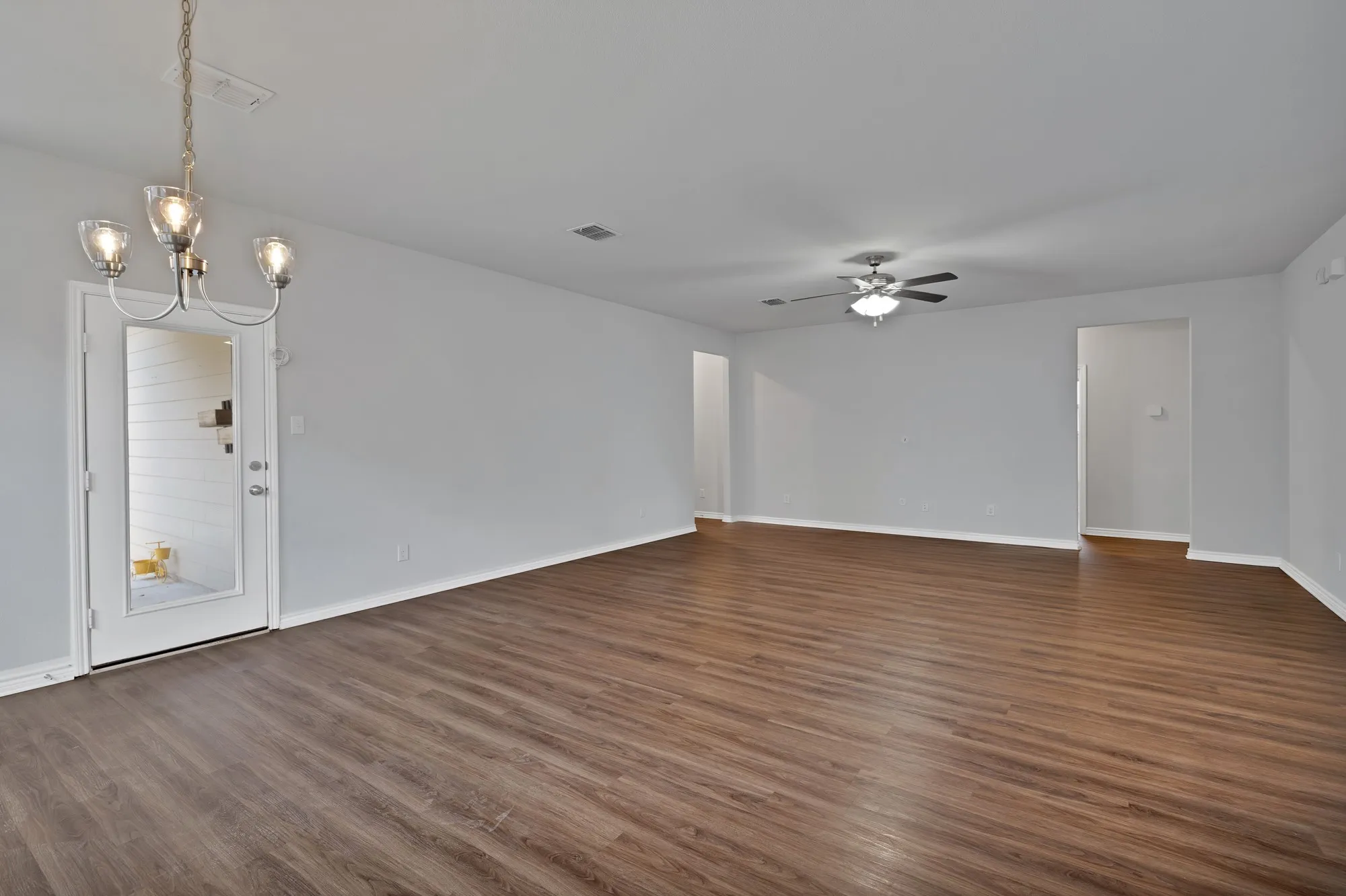 Empty room with a ceiling fan, dark wood finished floors, and a chandelier