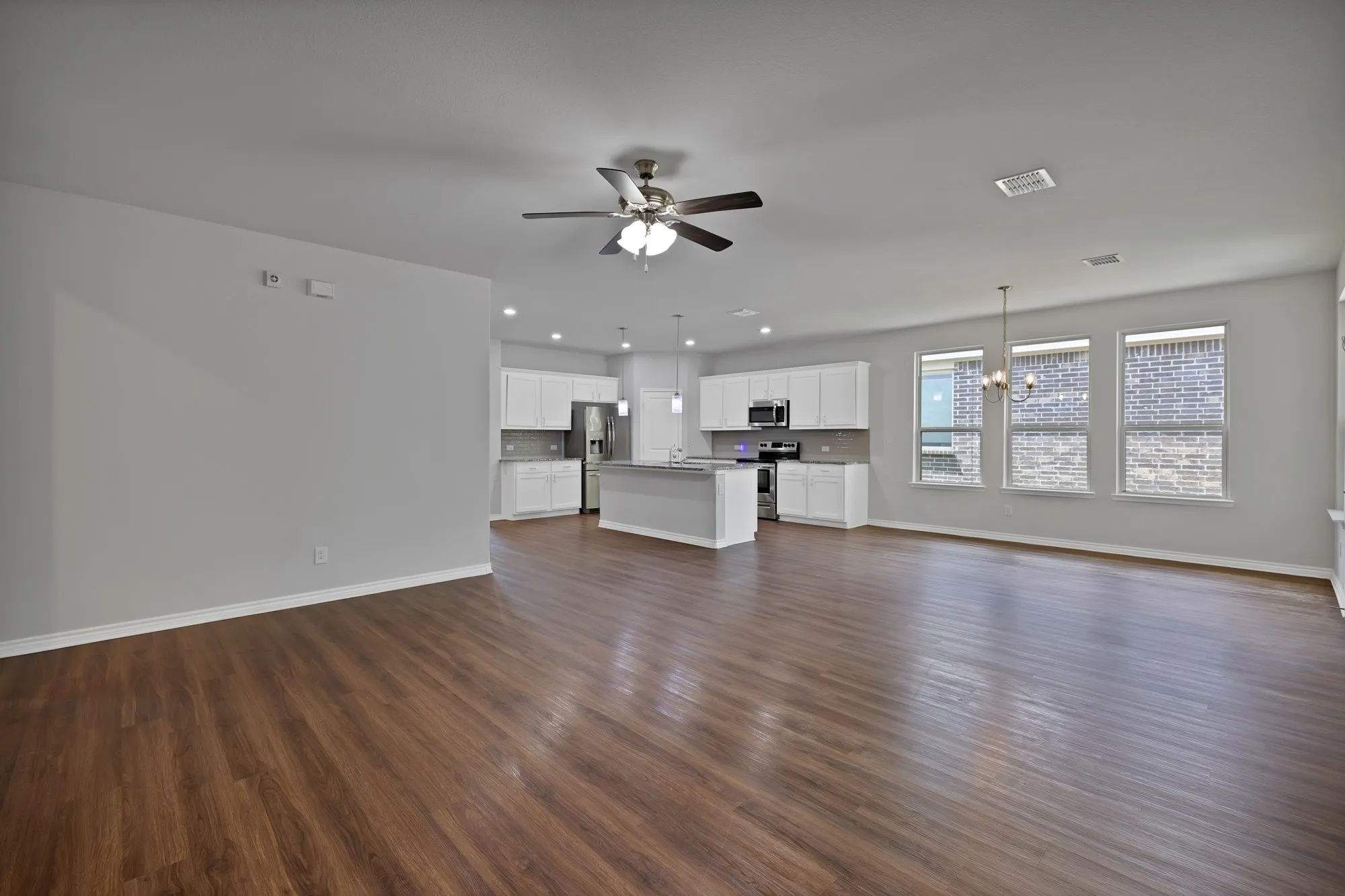 Unfurnished living room featuring ceiling fan, a chandelier, dark wood-style flooring, and recessed lighting