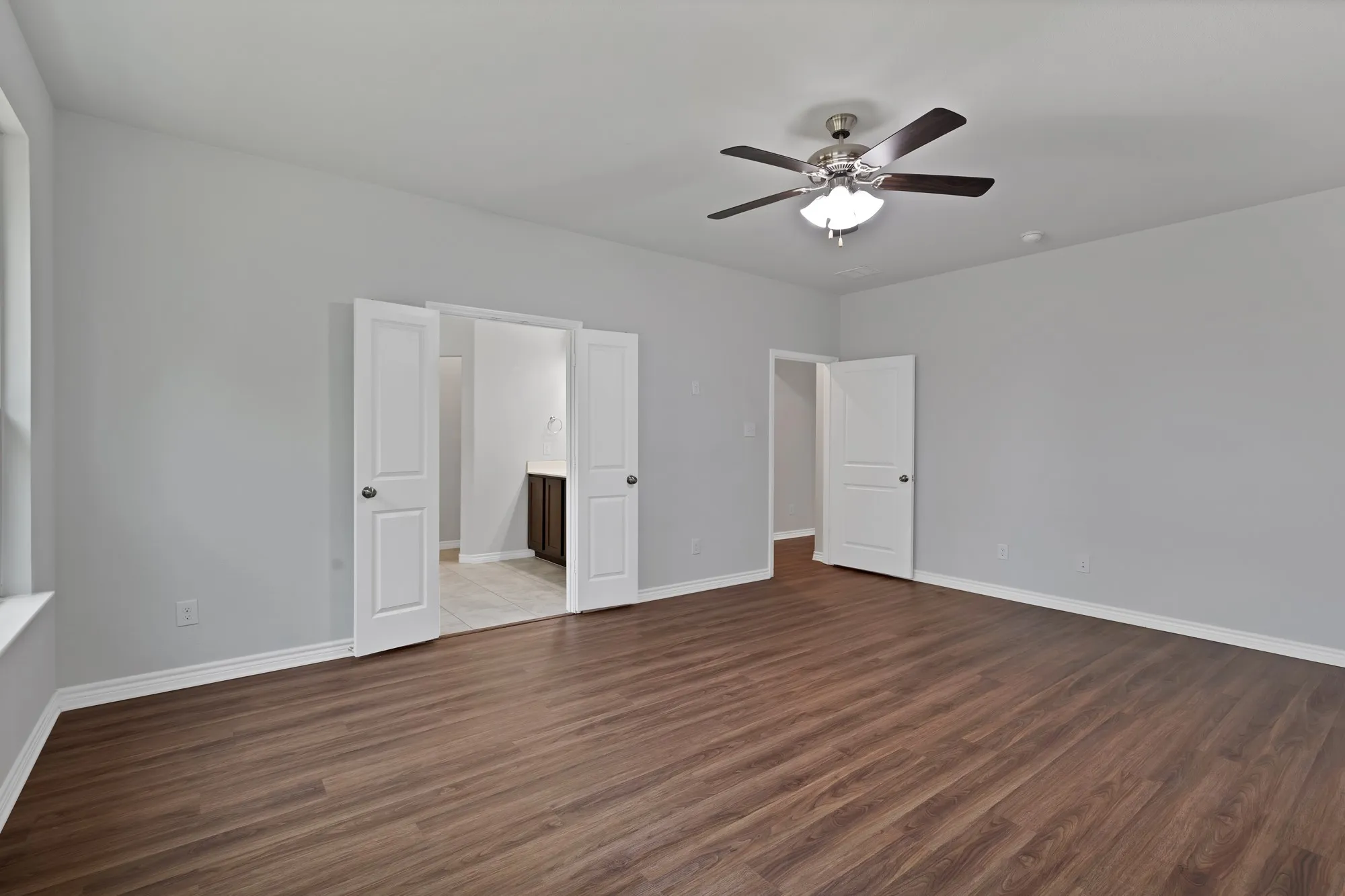 Unfurnished bedroom featuring wood finished floors, ensuite bathroom, and ceiling fan