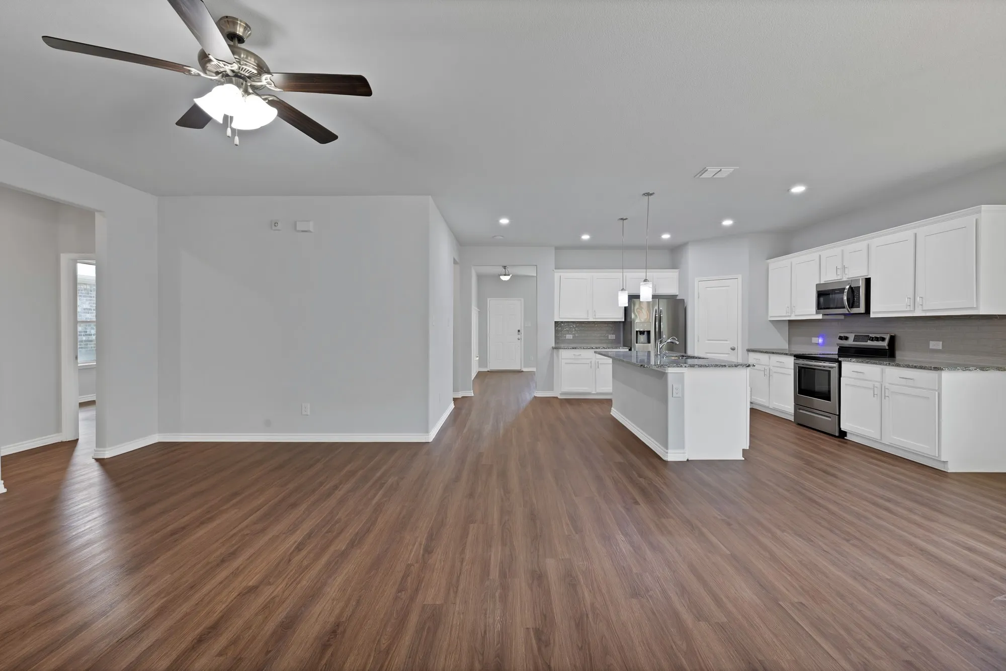 Kitchen with appliances with stainless steel finishes, open floor plan, decorative backsplash, ceiling fan, and dark wood finished floors