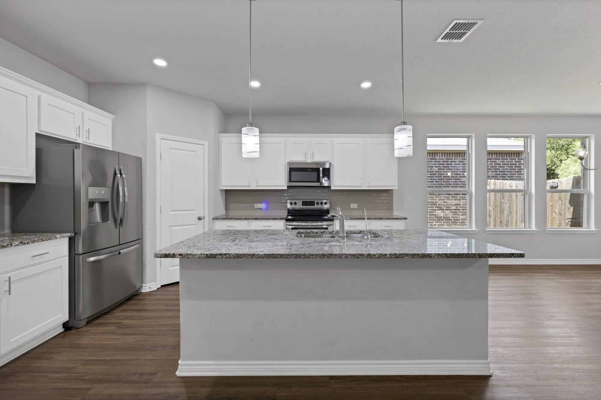 Kitchen with appliances with stainless steel finishes, dark wood-style flooring, stone countertops, white cabinetry, and recessed lighting