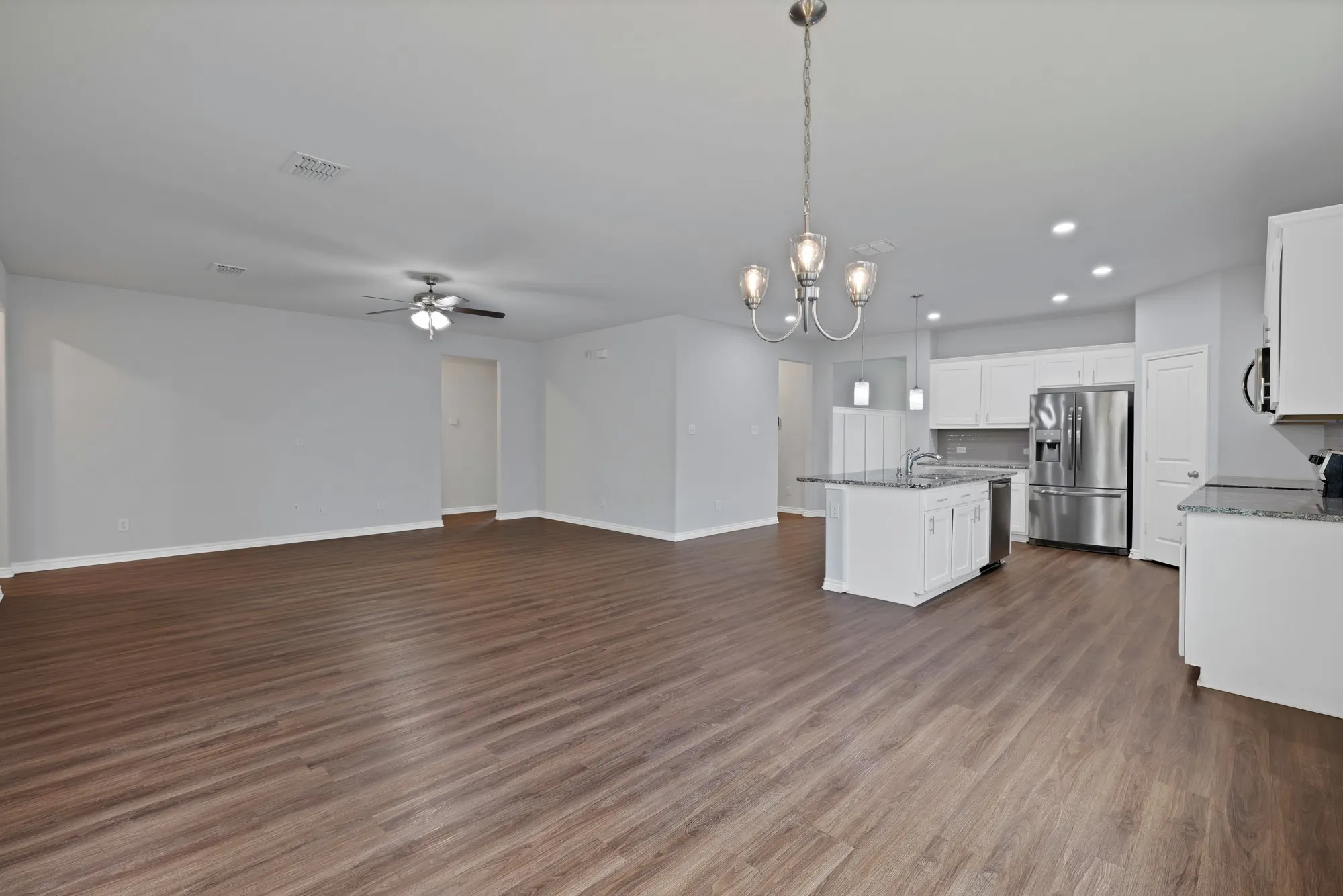 Kitchen with stainless steel appliances, open floor plan, a ceiling fan, a chandelier, and white cabinets