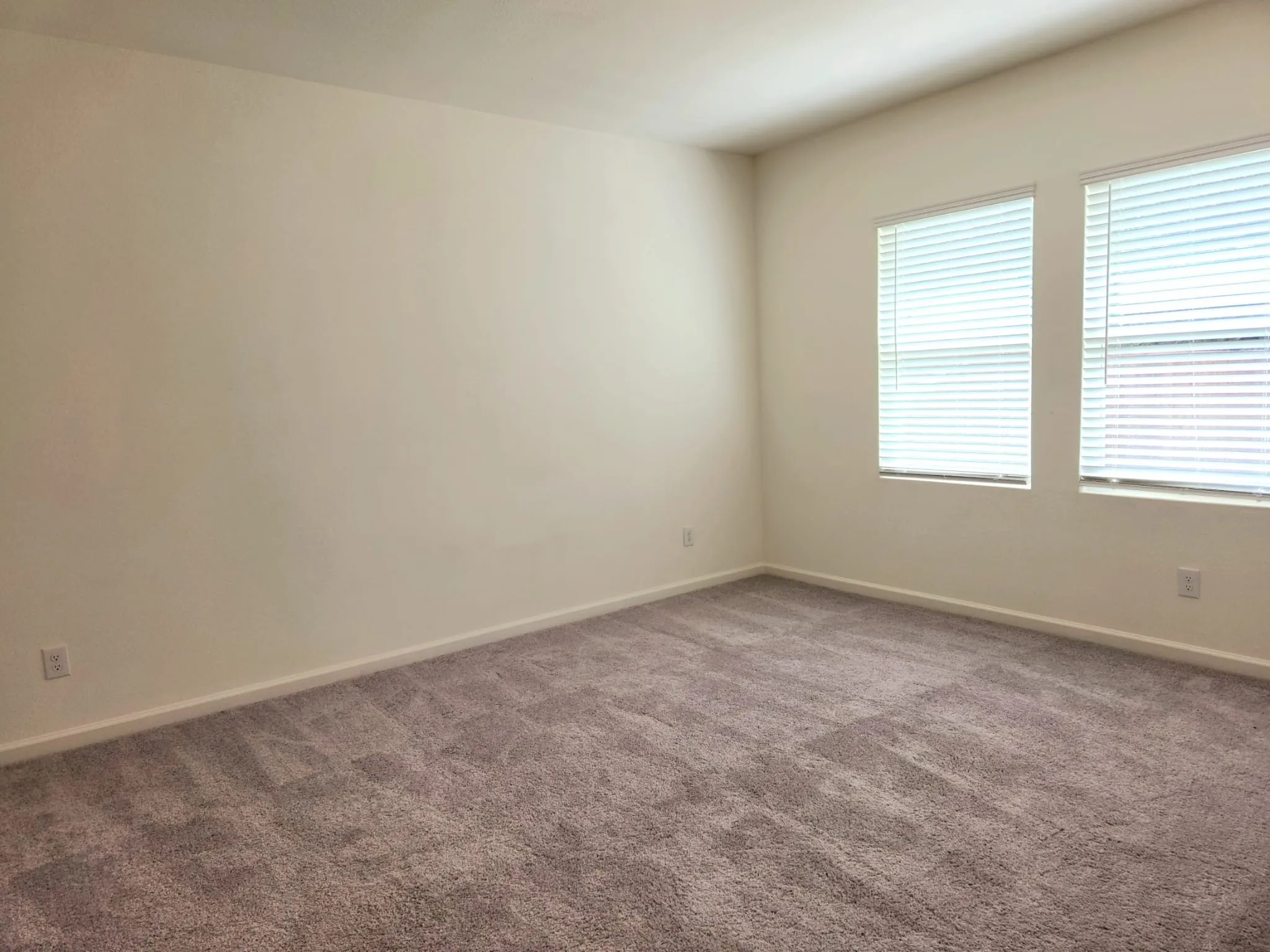 Neutral painted walls, vaulted ceiling, two windows with blinds, and carpet flooring