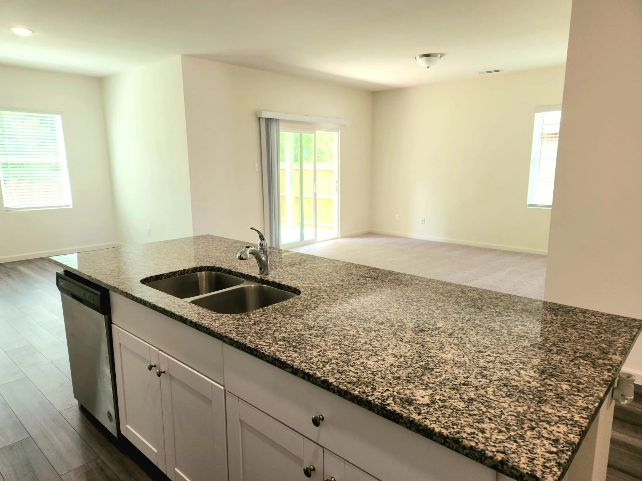 Kitchen island with granite countertop, stainless steel sink, and white cabinetry