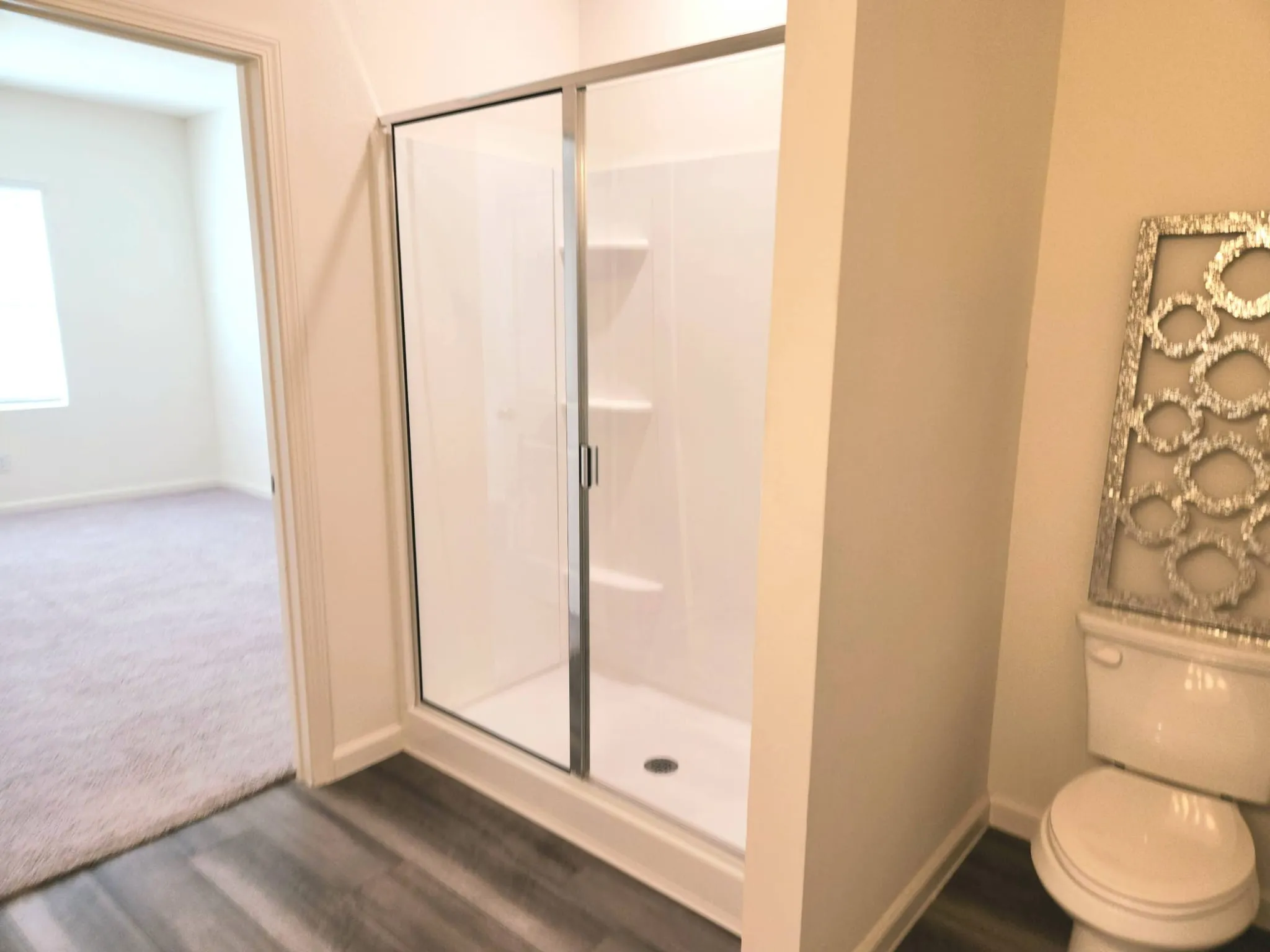 Enclosed shower with clear glass door, built-in shelving, and wood-finish flooring