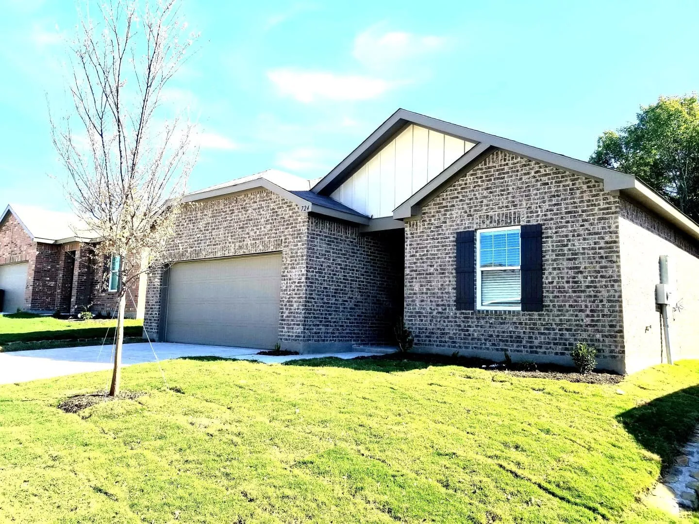 Brick exterior with white vertical siding accents, an attached garage, a paved driveway, and a manicured lawn