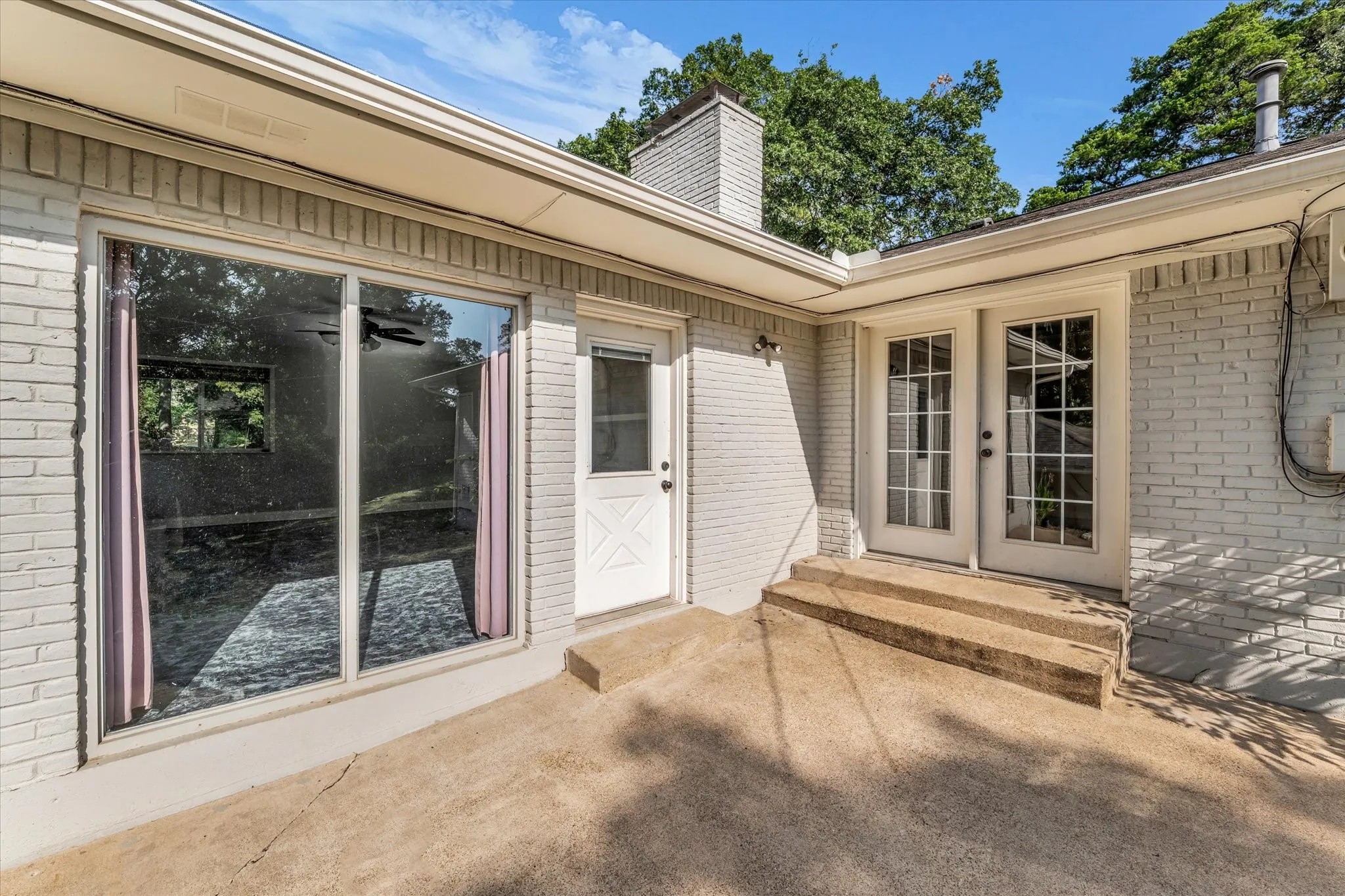 Brick exterior with concrete patio, featuring a sliding glass door and French doors