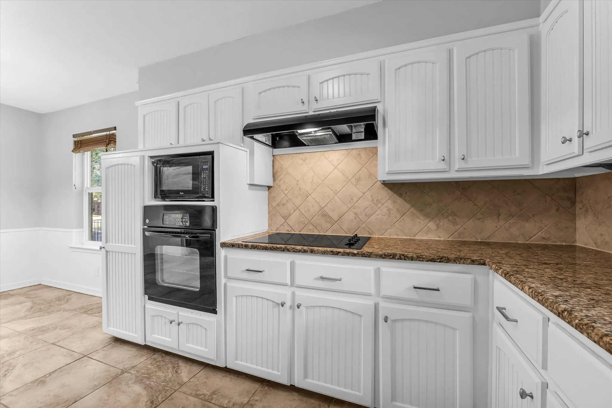White cabinetry, built-in oven and microwave, dark brown granite countertops, diagonal tile backsplash, and ceramic tile flooring