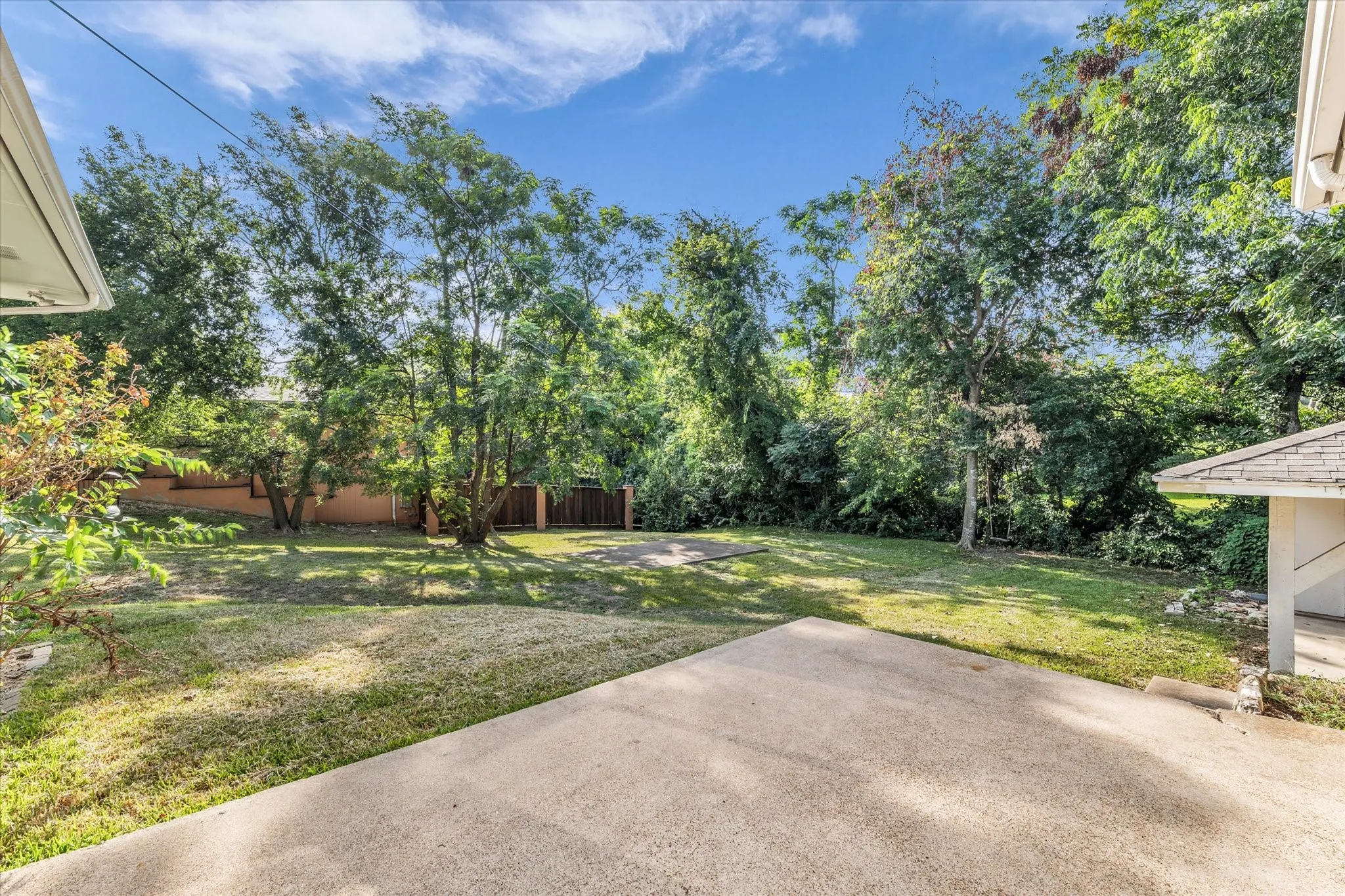 Expansive backyard featuring a concrete patio, mature trees, and a level lawn