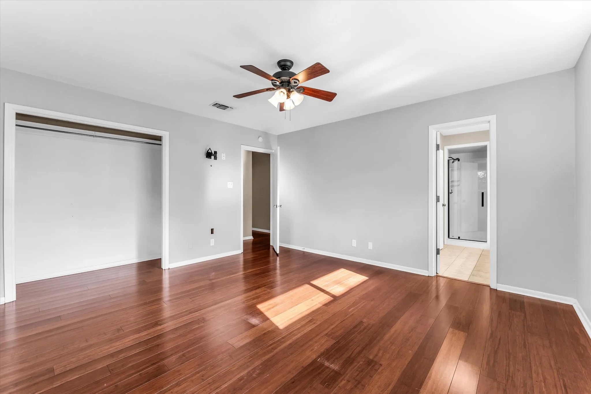 Wood-finish flooring, ceiling fan with integrated lighting, recessed closet, and light gray wall paint. Ensuite bathroom