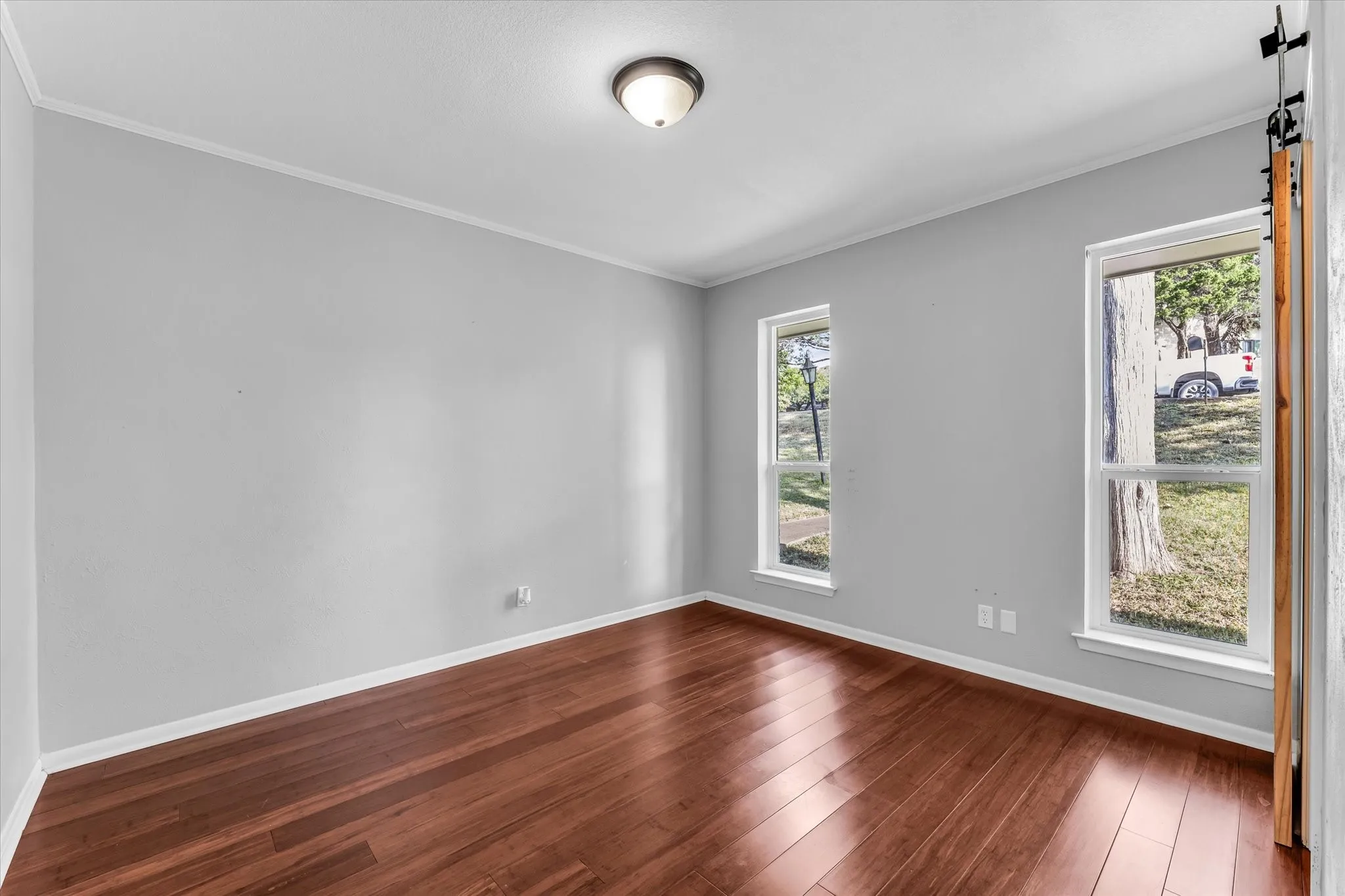 Wood-finish flooring, light gray walls, two windows, and a flush-mount ceiling light fixture