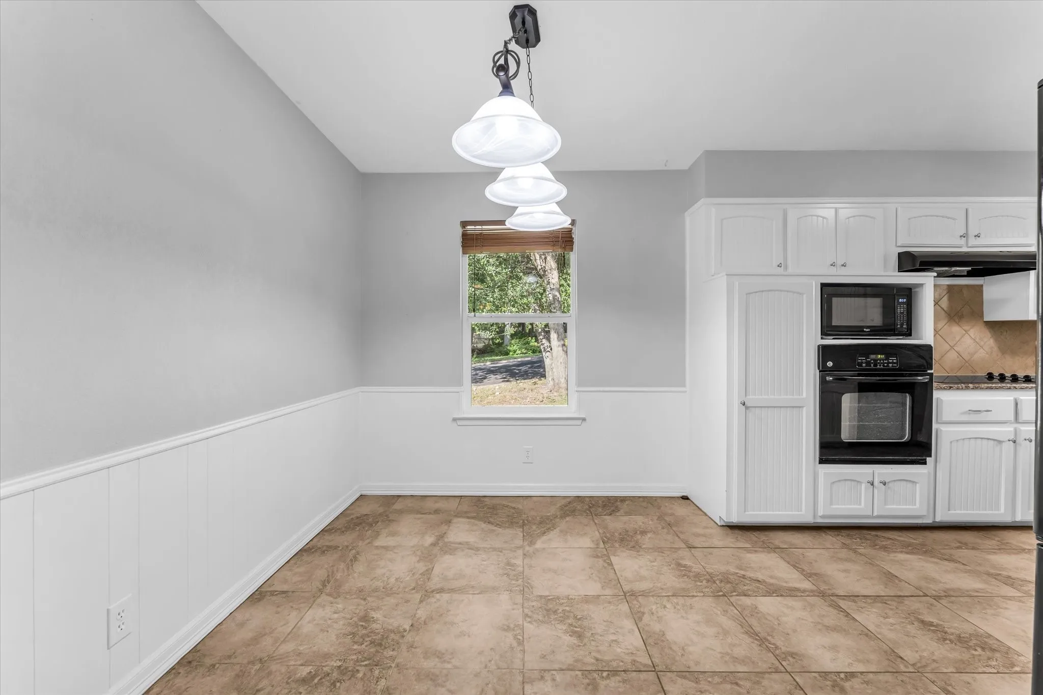 Built-in wall oven and microwave, white cabinetry, tile flooring, and wall wainscoting