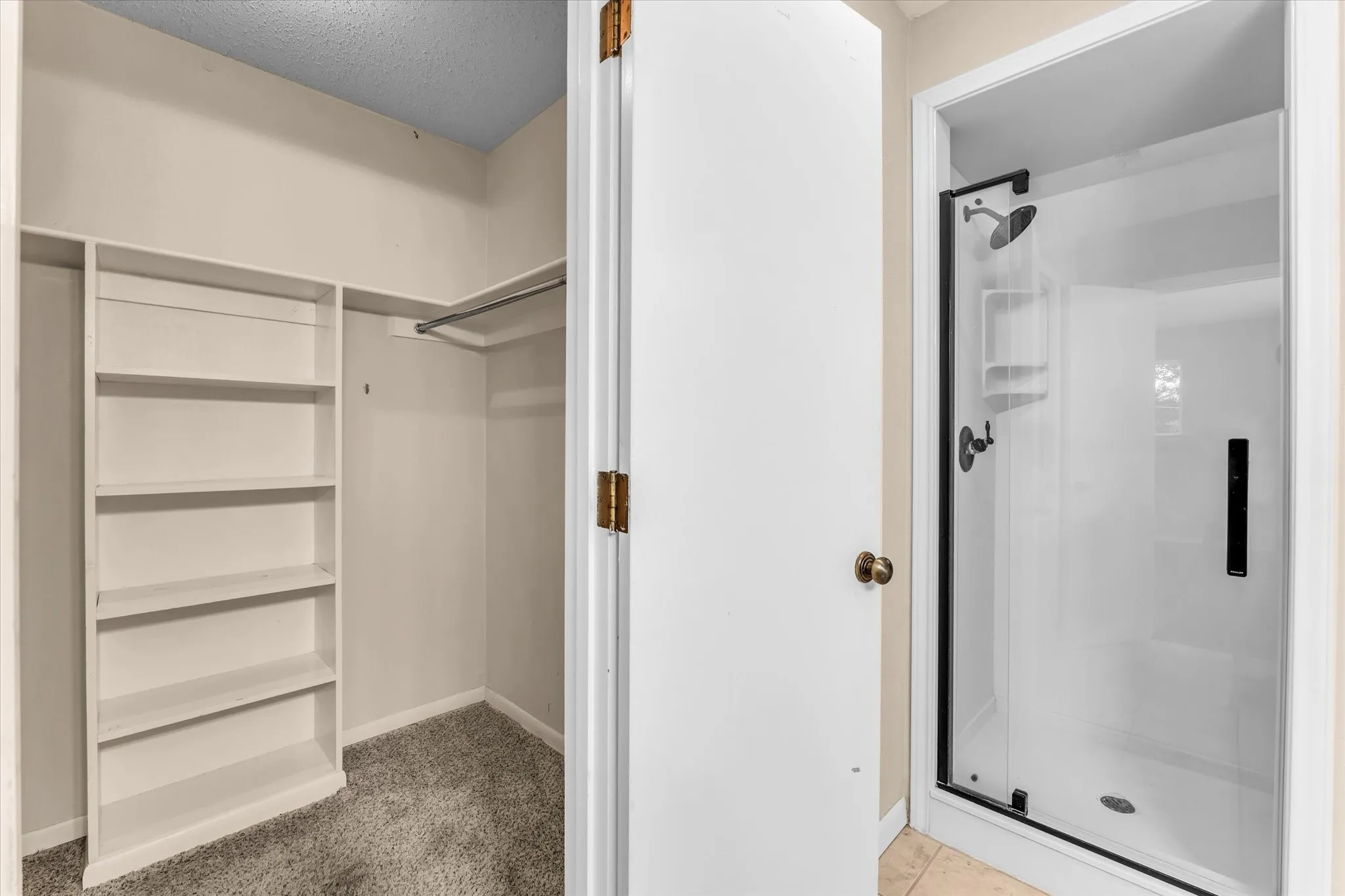 Built-in shelving, closet rod, and enclosed shower with a black-framed glass door, and black shower fixtures