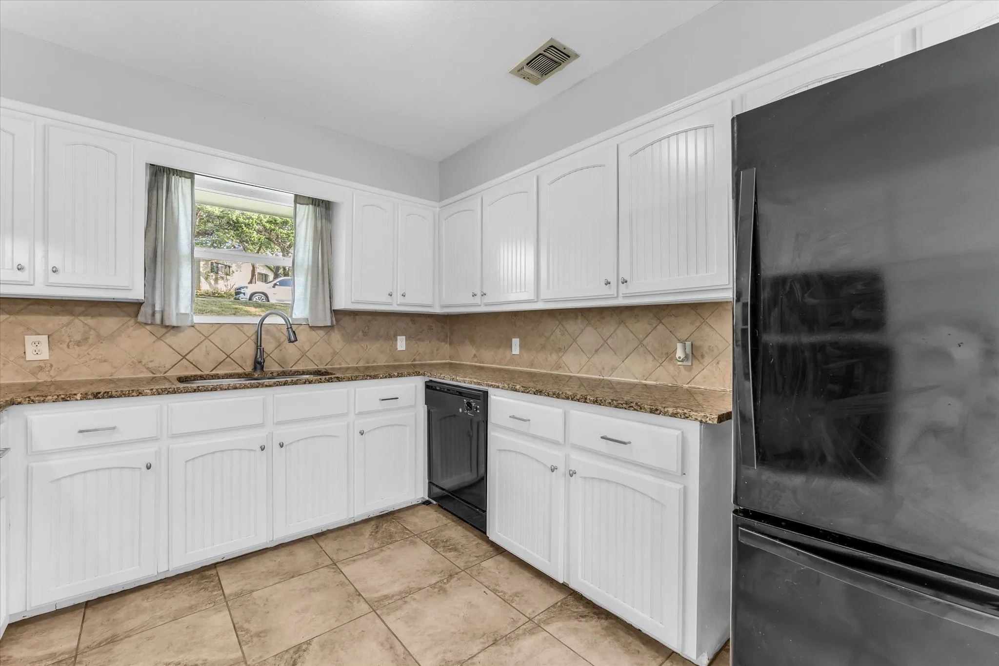 White cabinetry, stone countertops, tile flooring, tile backsplash, and a stainless steel sink with a gooseneck faucet