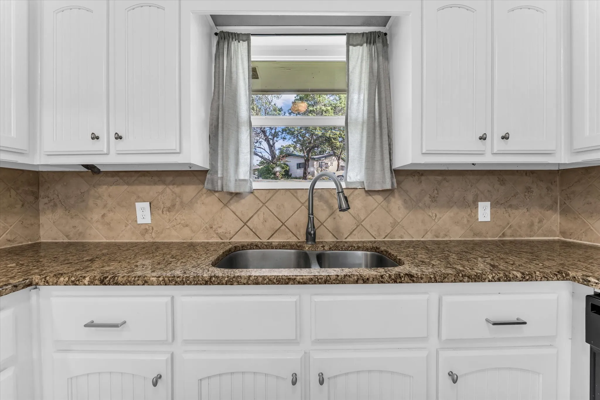 White cabinetry, dual basin stainless steel sink, gooseneck faucet, tiled backsplash, and granite countertops