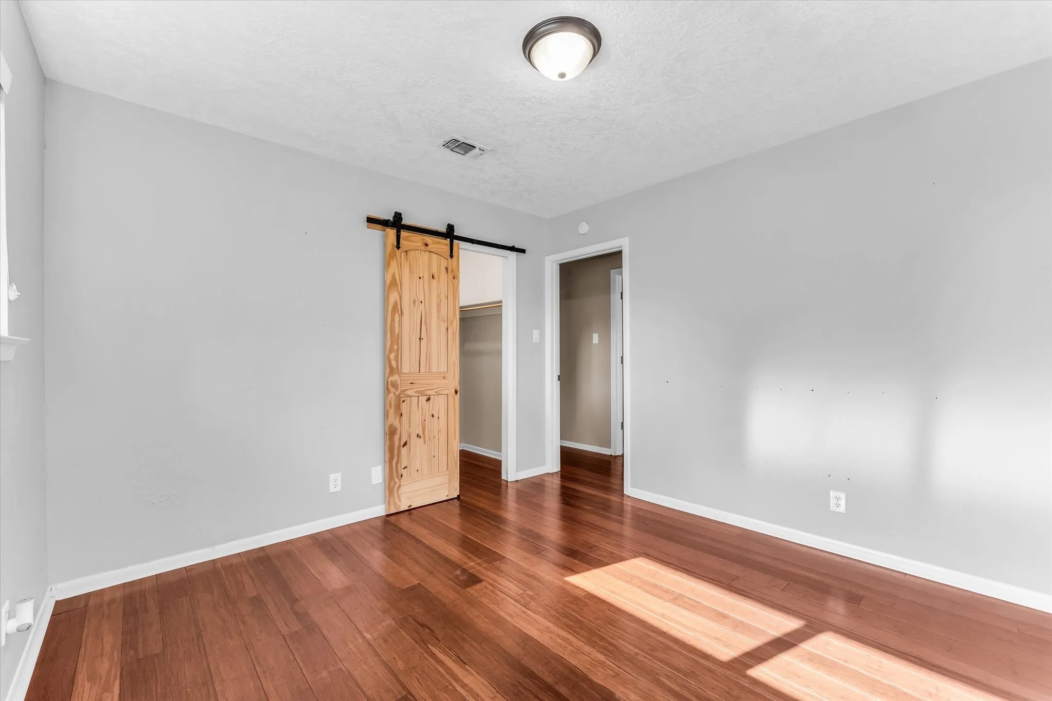 Hardwood flooring throughout, light gray wall paint, and a wood-finish barn door
