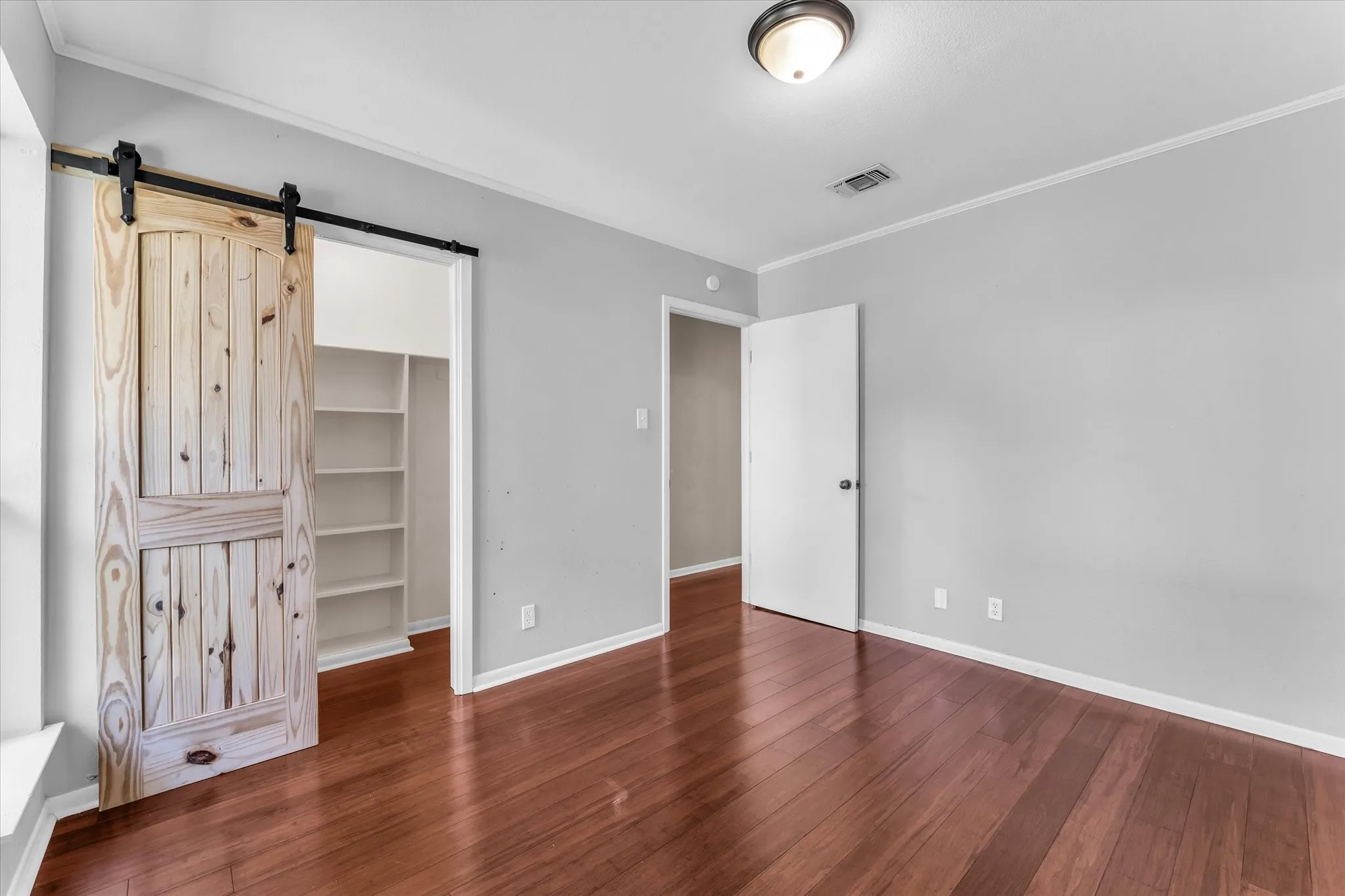 Rich wood-finish flooring, light gray wall paint, and a wood-panel barn door with a black track system