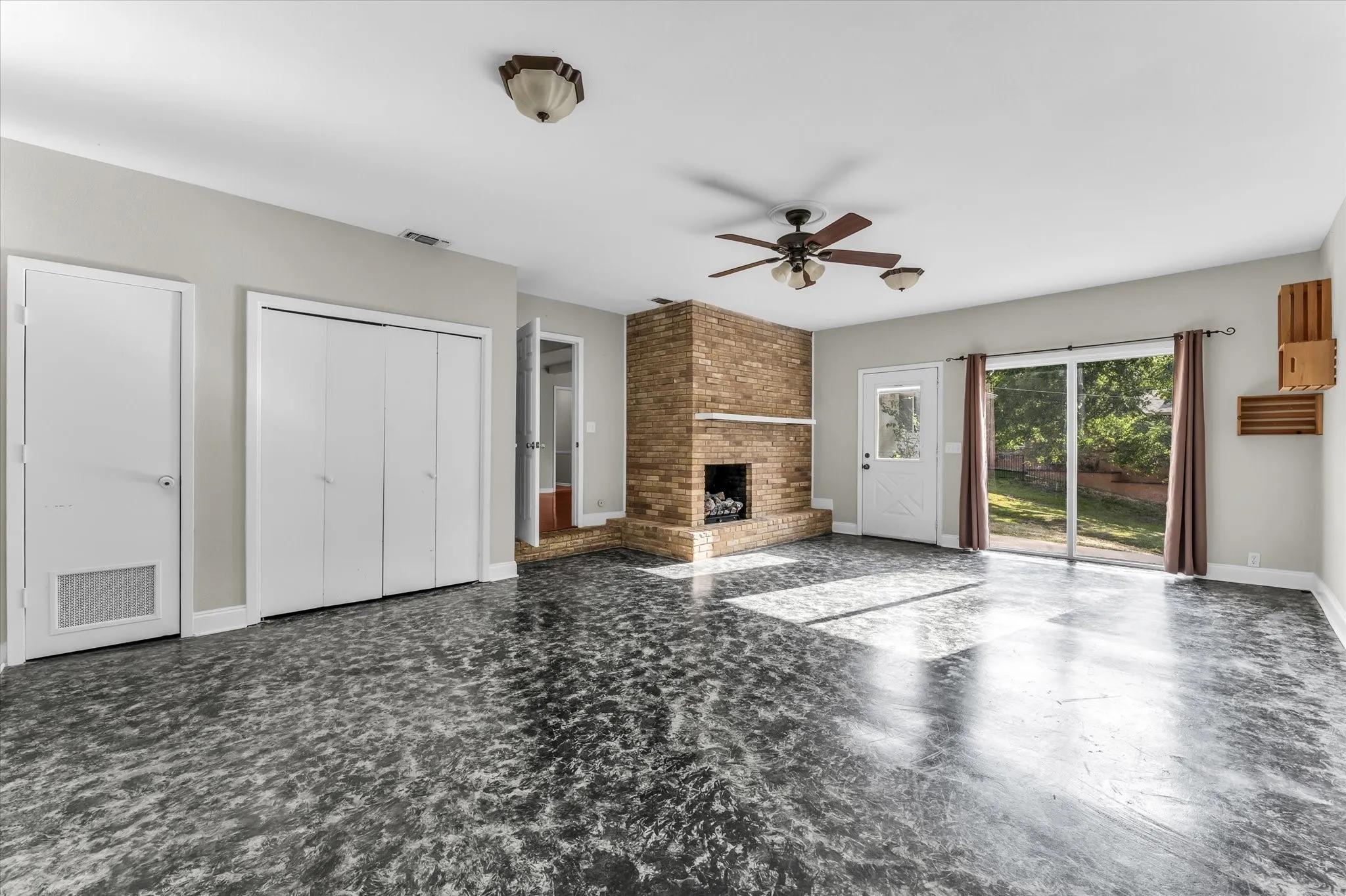Spacious room with a brick fireplace (shared with livingroom), sliding glass doors and exterior door, and a ceiling fan