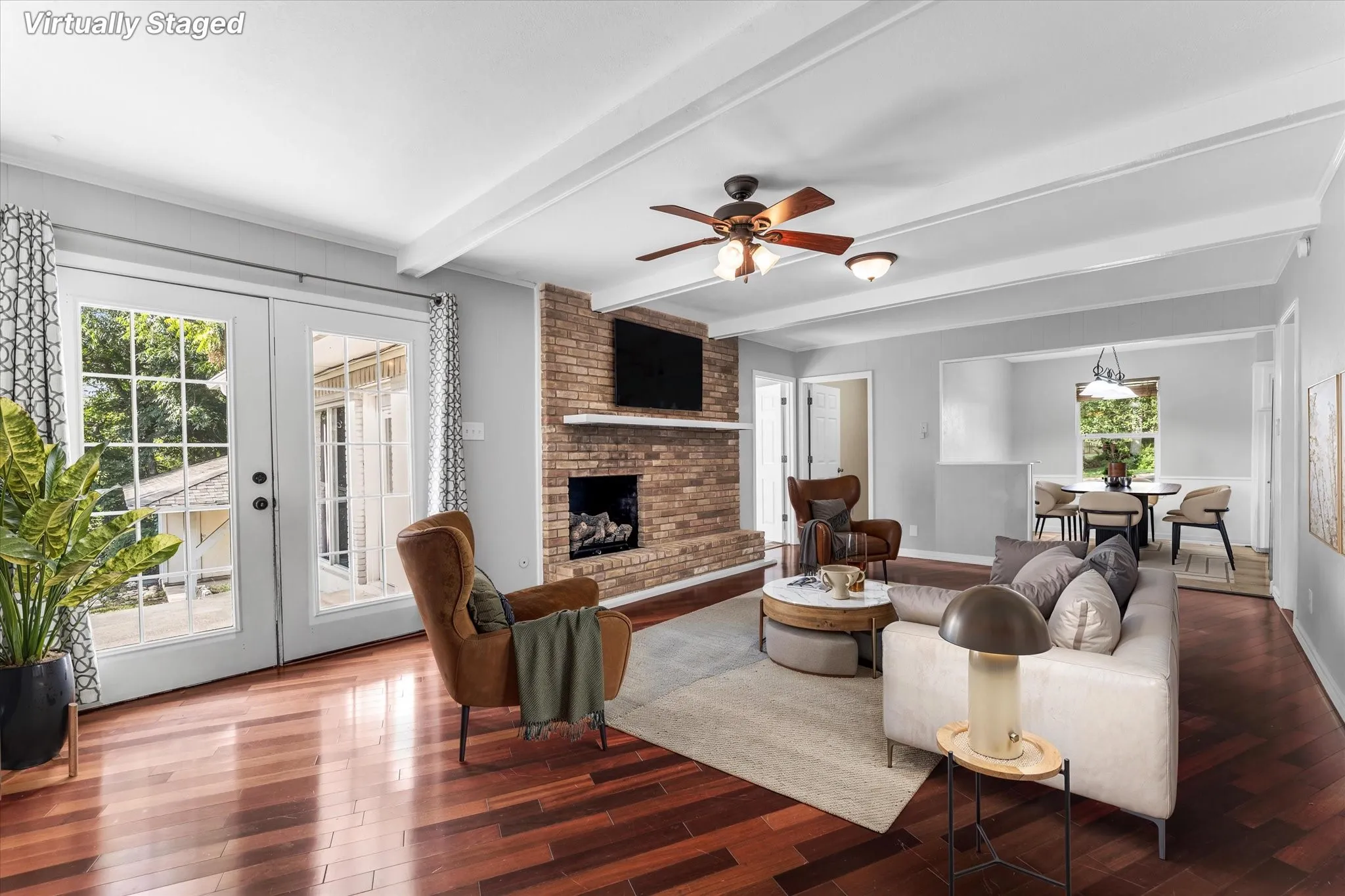 Expansive living area with wood-finish flooring, a brick fireplace, and beamed ceilings