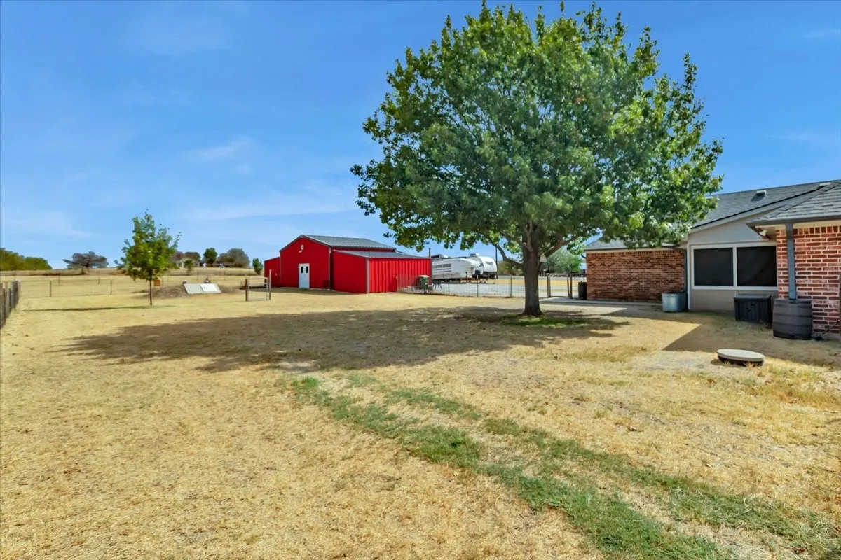 Expansive outdoor space featuring a detached red barn, fenced perimeter, and mature trees