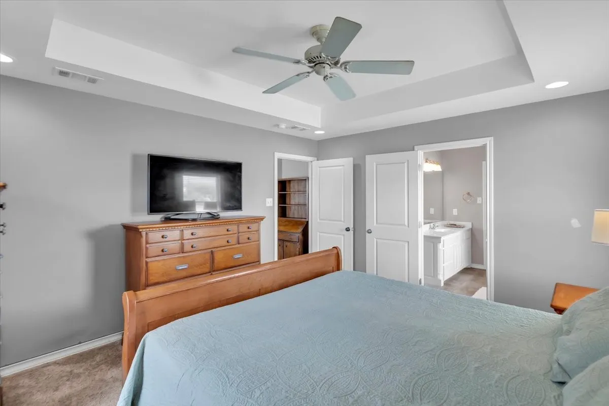 Tray ceiling with recessed lighting and a ceiling fan, plush carpet, and a white paneled door