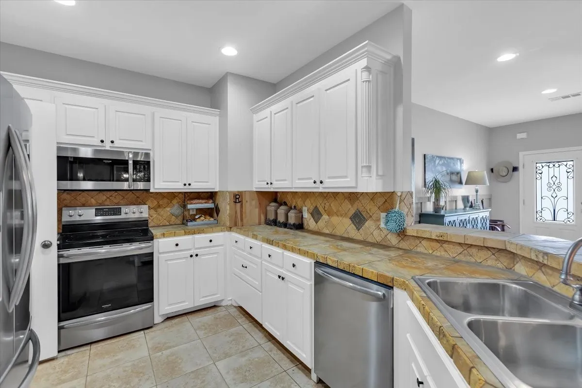 Kitchen featuring white cabinetry, tile flooring, stainless steel appliances, and a tiled backsplash